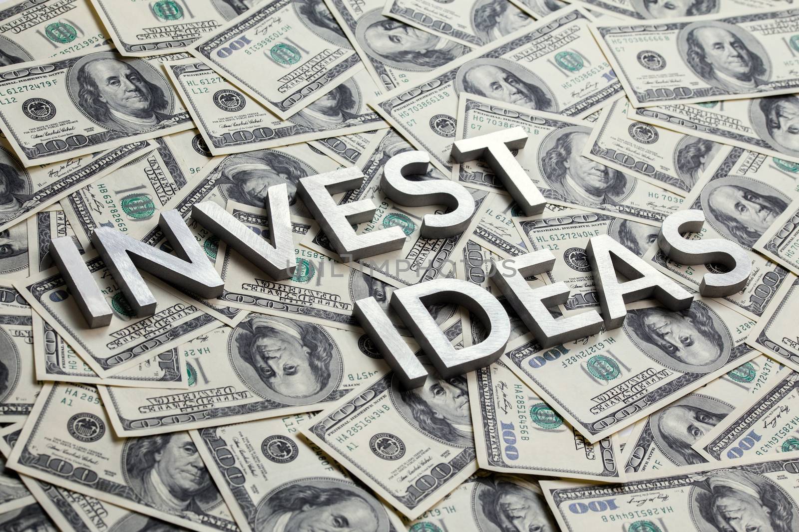 The words INVEST IDEAS laid with thick metal letters on the US dollar bills background - with selective focus and diagonal composition.