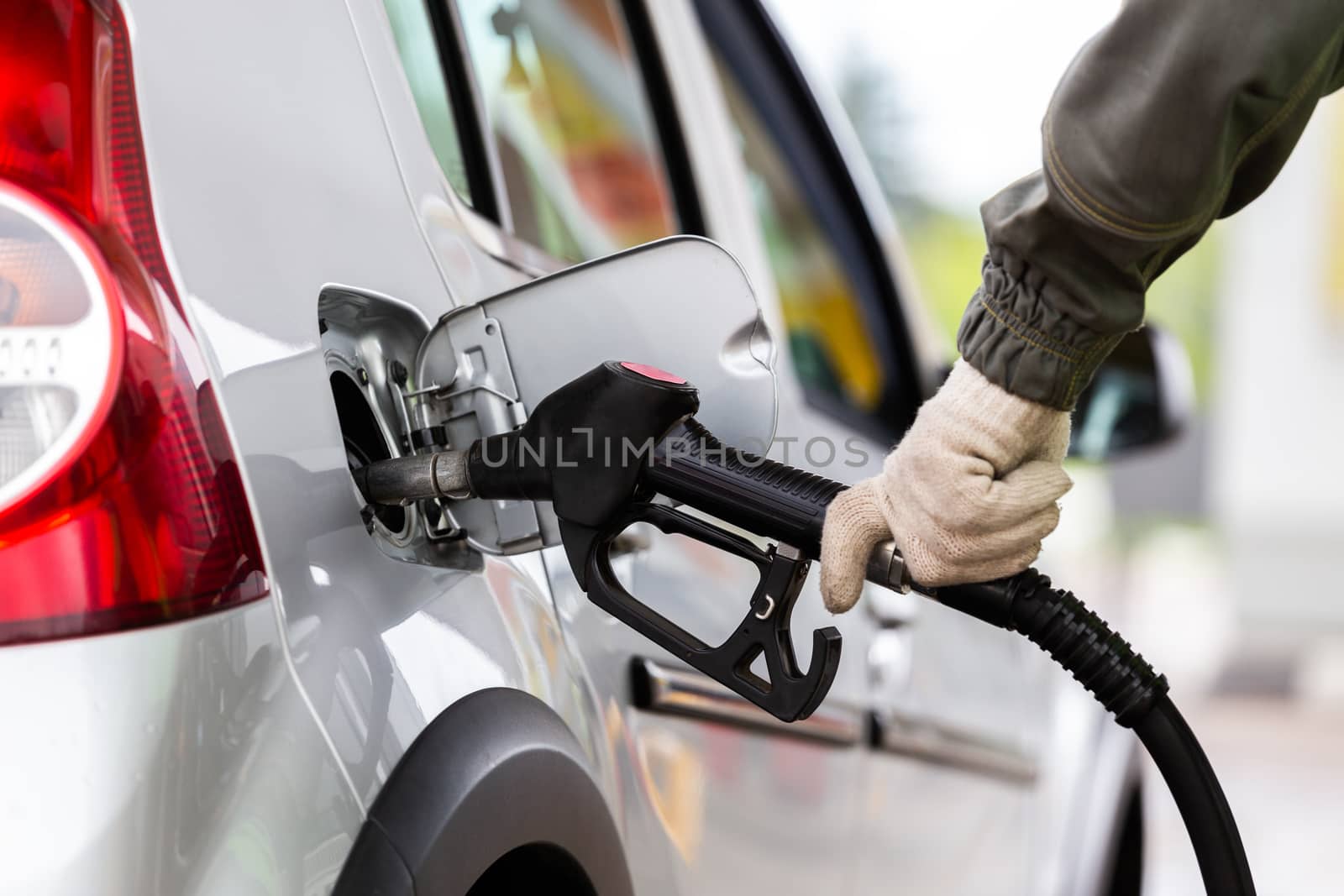 hand in white fabric glove refueling gray metallic car on gas station - closeup with selective focus and blur