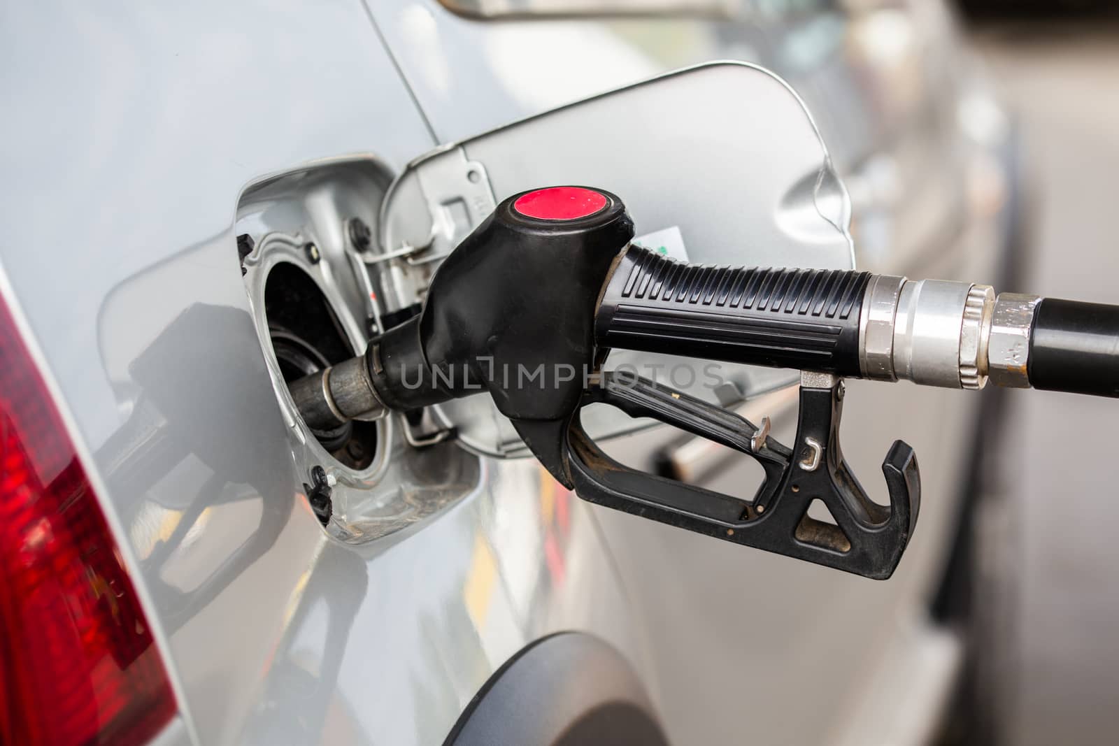 gray metallic car refueling on gas station - closeup with selective focus and blurry man on background.