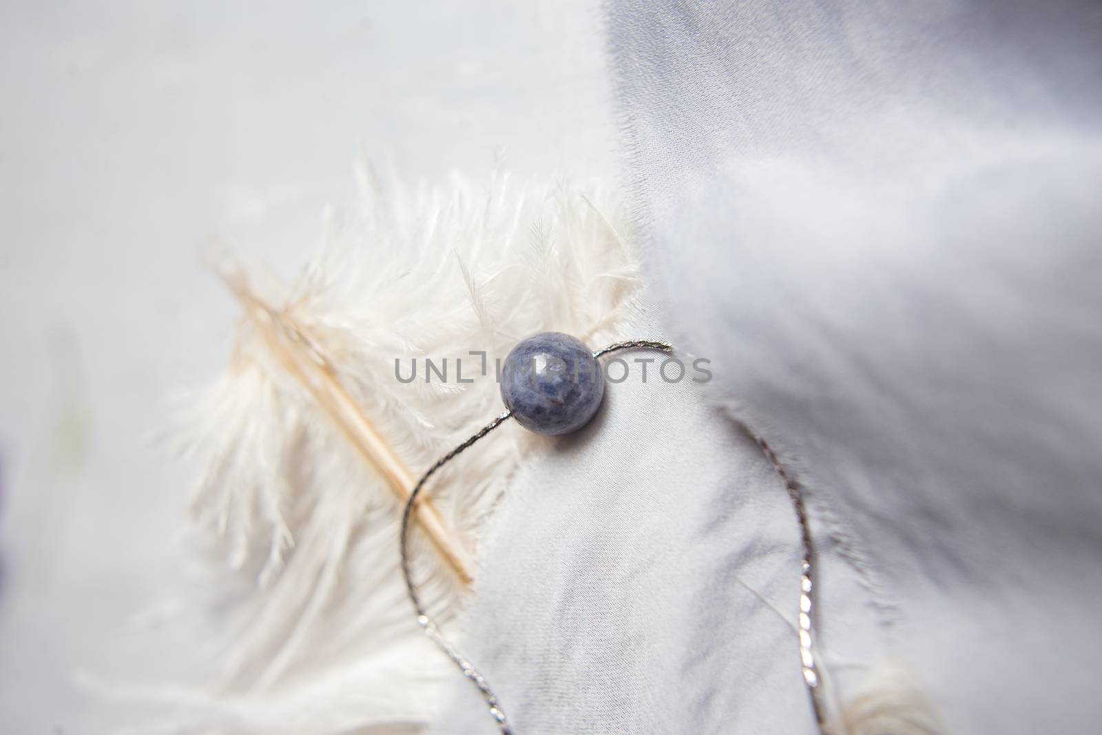 Original silver jewelry necklace made of natural stone with purple violet lilac flowers on white ostrich feather. Gift concept. Silver accessories. Mock up space for text.