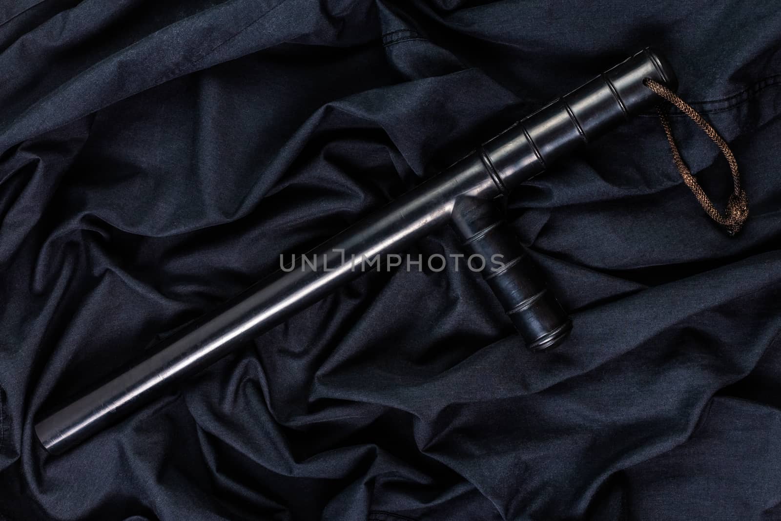 black rubber police baton on black shirt wrinkled cloth low-key flat lay.