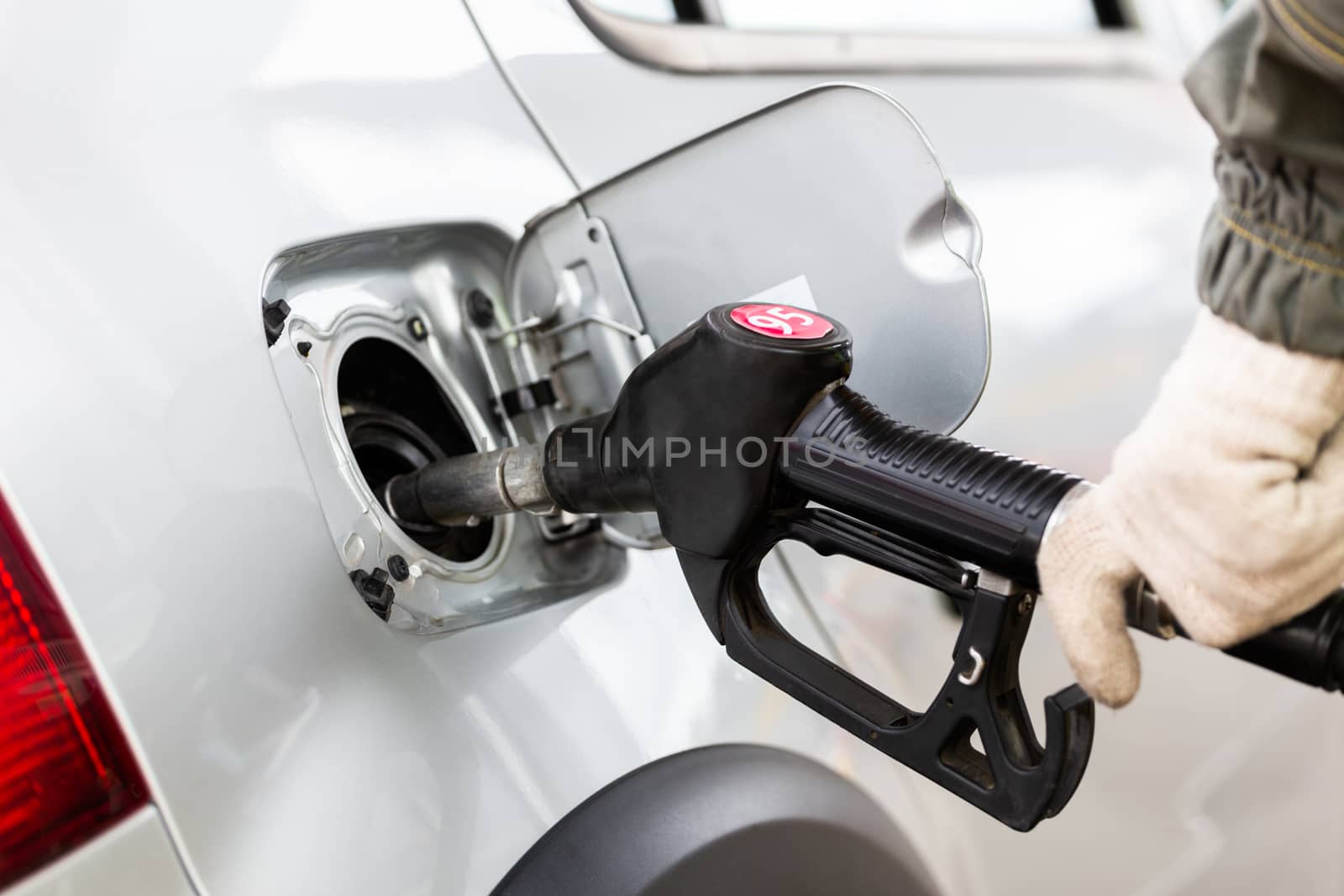 hand in white cotton fabric glove refueling gray metallic car on gas station - closeup with selective focus and blur