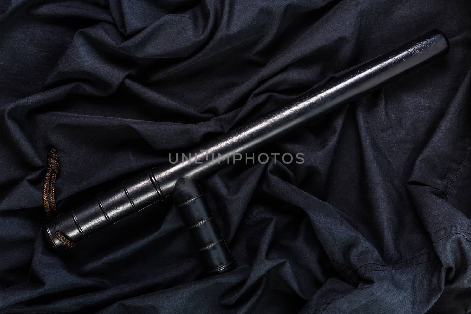 black rubber police baton on black shirt wrinkled cloth low-key flat lay.