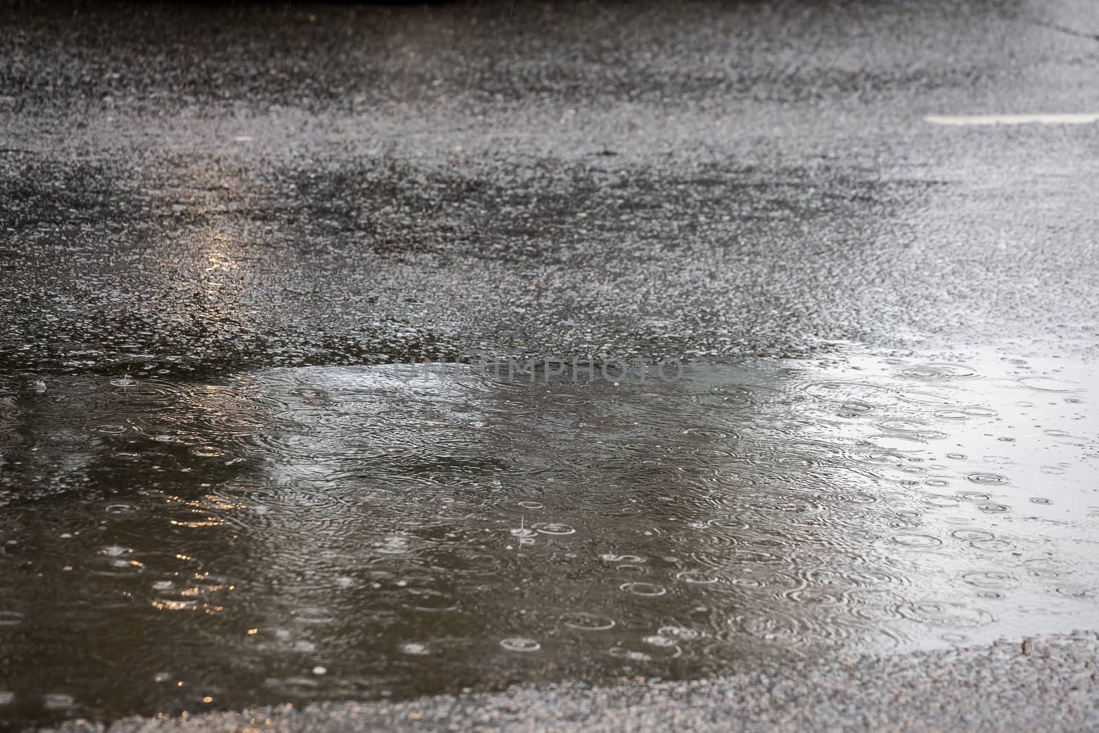 puddle on asphalt road at daylight rain in city with selective focus and boke blur.
