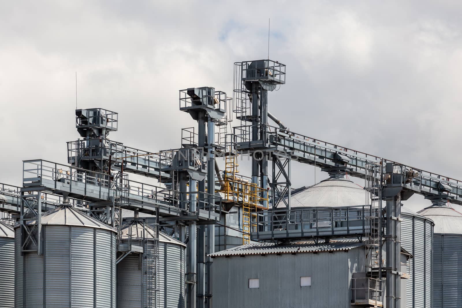 metal grain silos with elevator loading clonstructions at cloudy daylight.