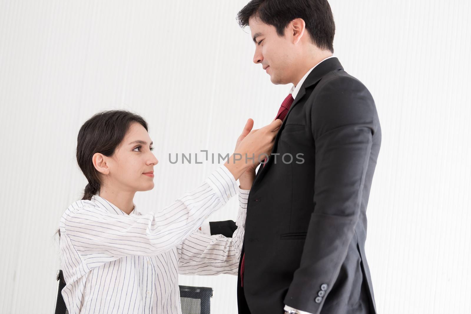 Wife tying red necktie to her husband in the office with smiling by animagesdesign
