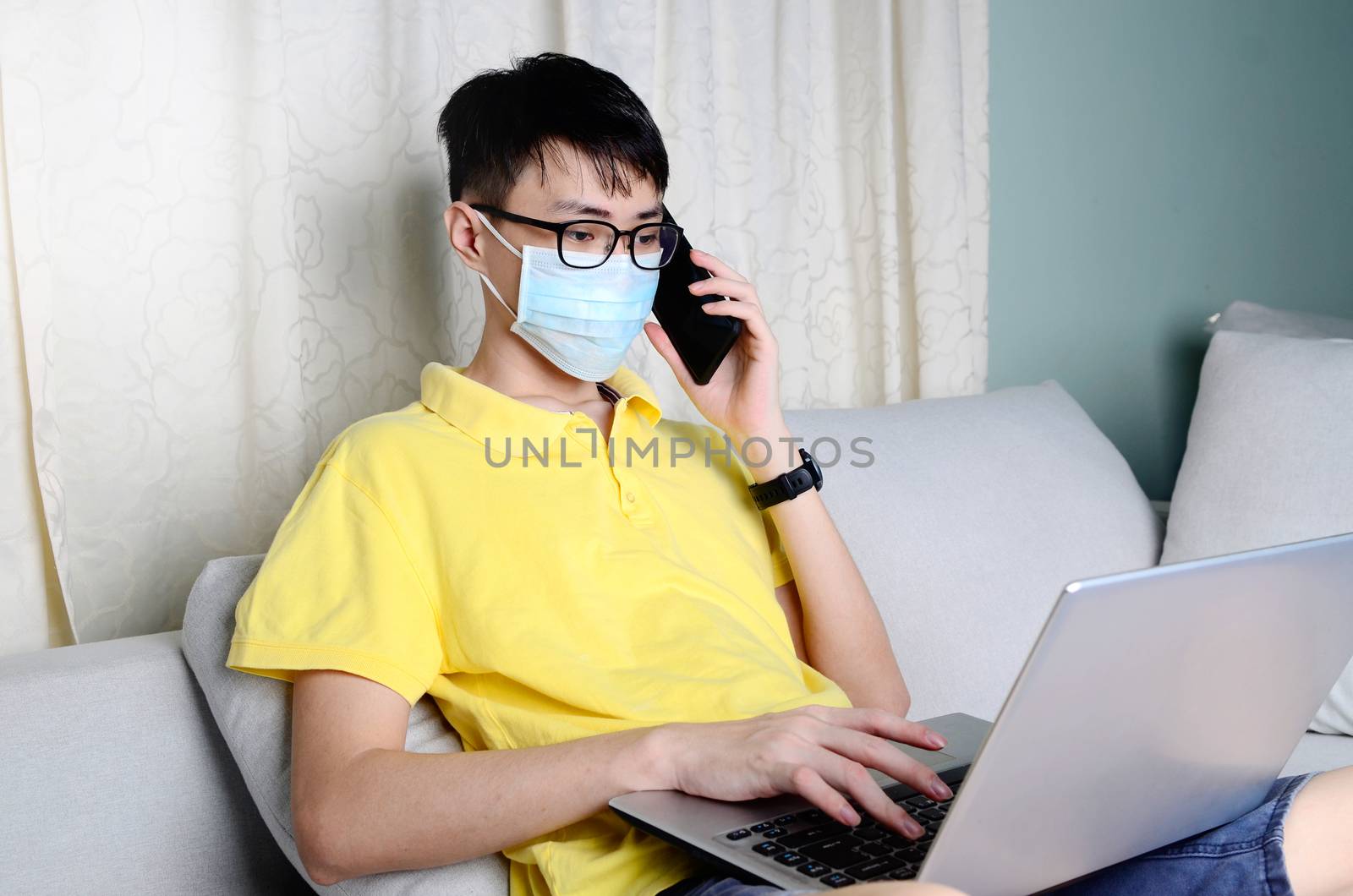 An asian man is working from home during pandemic coronavirus  Covid-19. Ccoronavirus covid 19 infected patient in quarantine room using smartphone and  computer.



