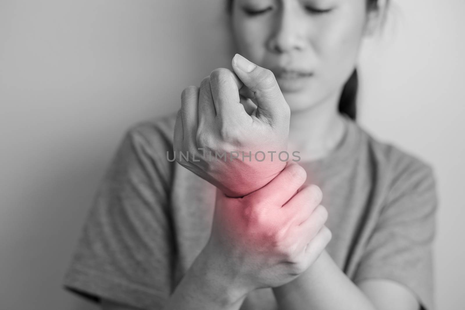Woman suffering from pain in wrist. Pain in a women wrist. Young woman holding her painful wrist on wall background.