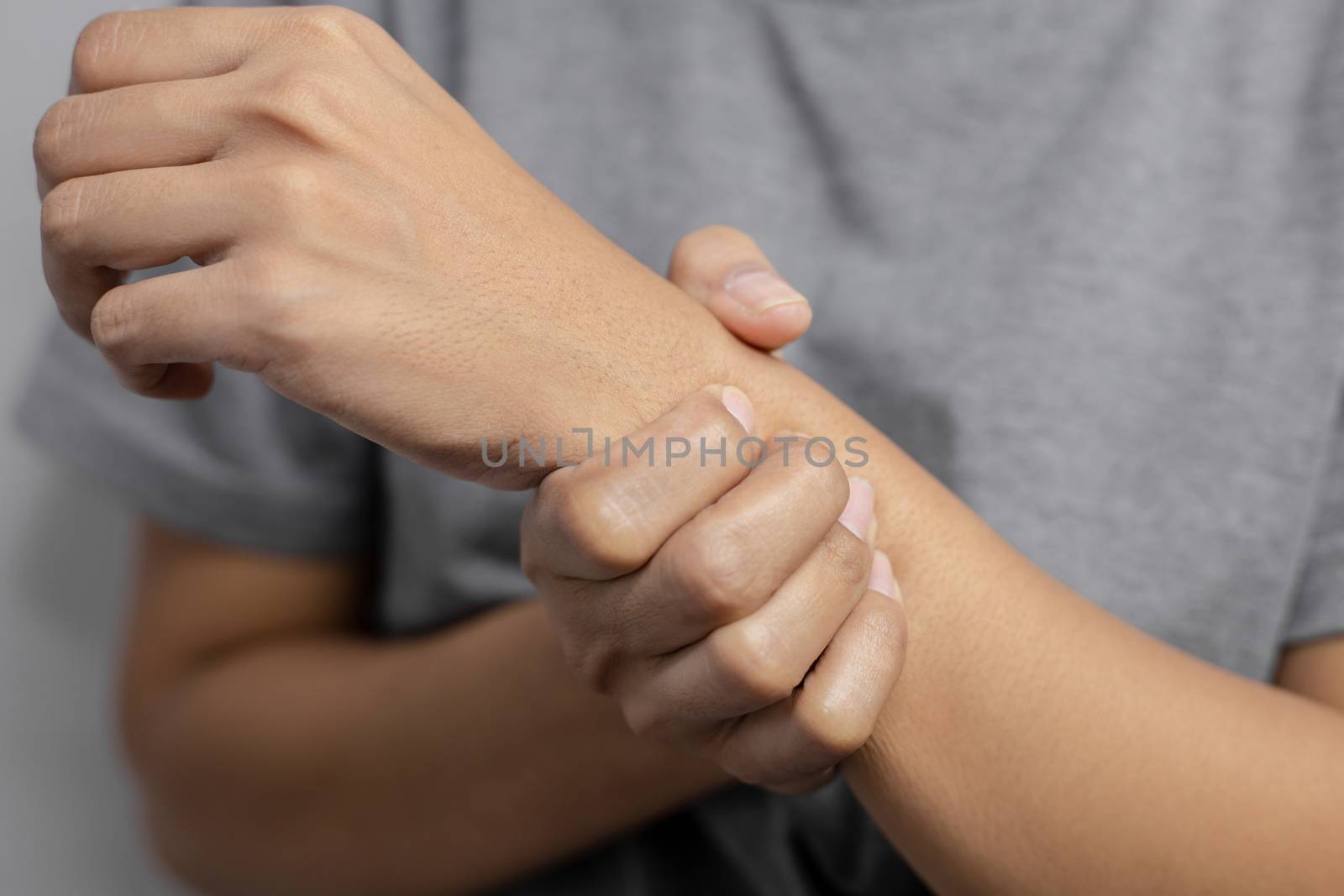 Woman suffering from pain in wrist. Pain in a women wrist. Young woman holding her painful wrist on wall background.