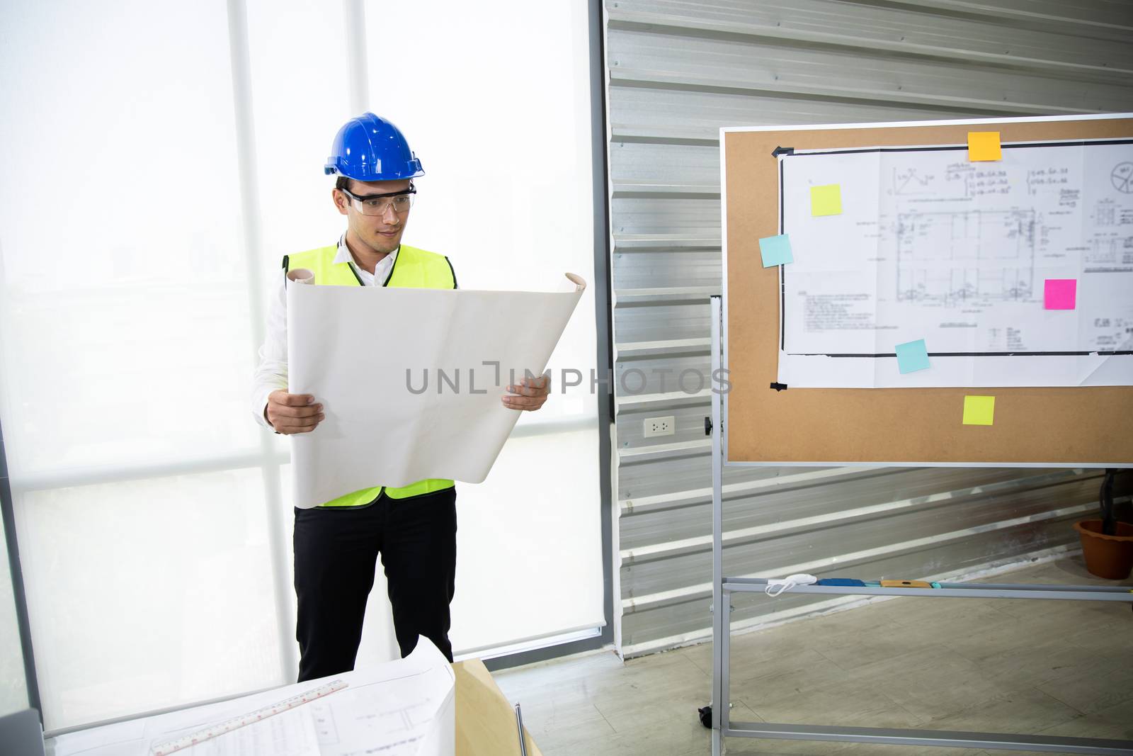 Young man engineer who stood to watch the project structure with the intention in office. Male industrial engineers look at project blueprints in the factory. Engineer and business work concept .