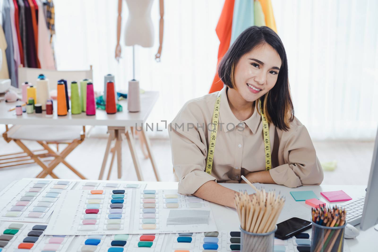Asian woman designer are thinking and designing clothes for customers order items at the designer desk in the studio. Clothes designers are working in the office. Startup designer concept.
