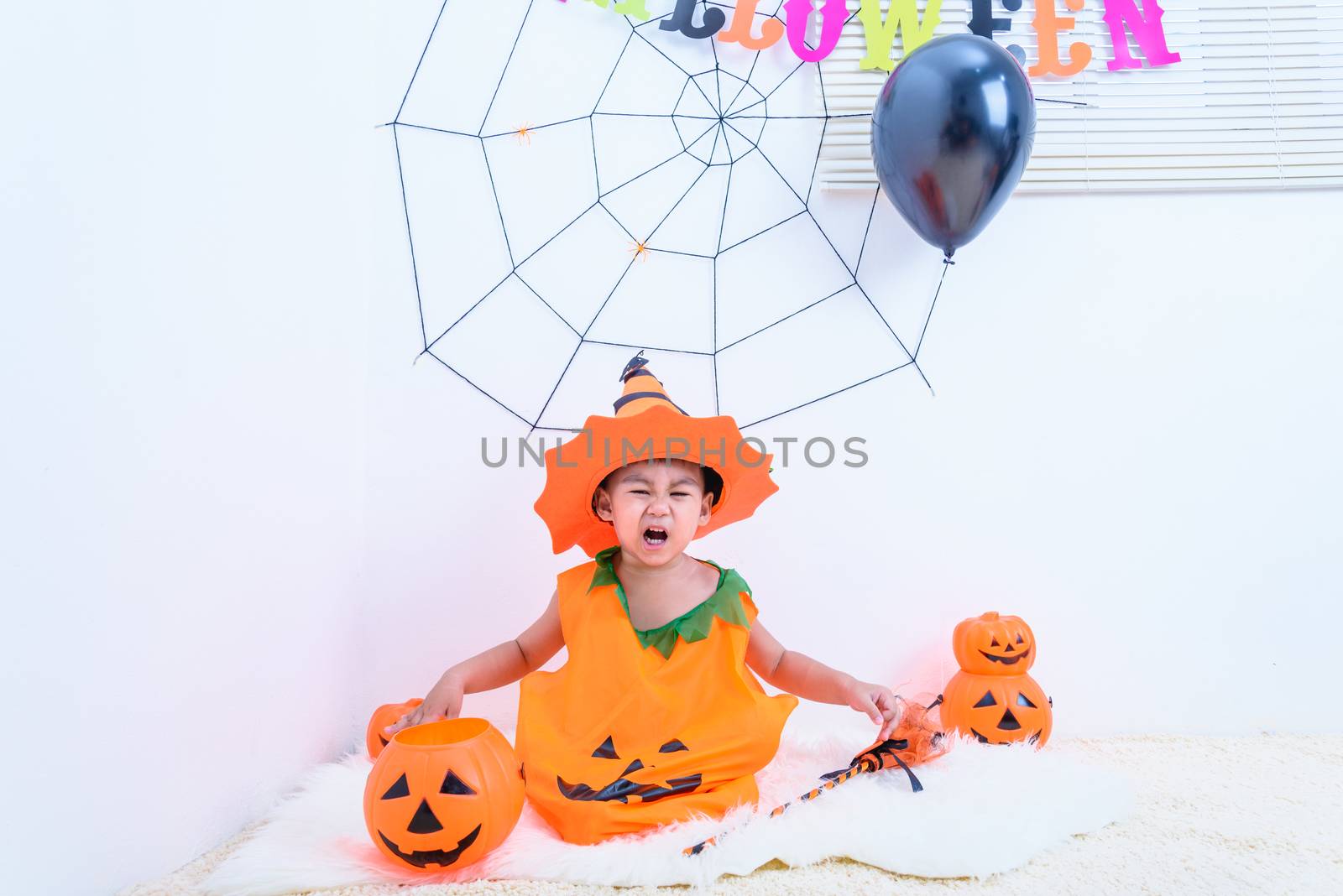The little cute boy Kid on Halloween costume orange pumpkin he sitting in Halloween party house and open mouth for horror, Happy Halloween day concept

