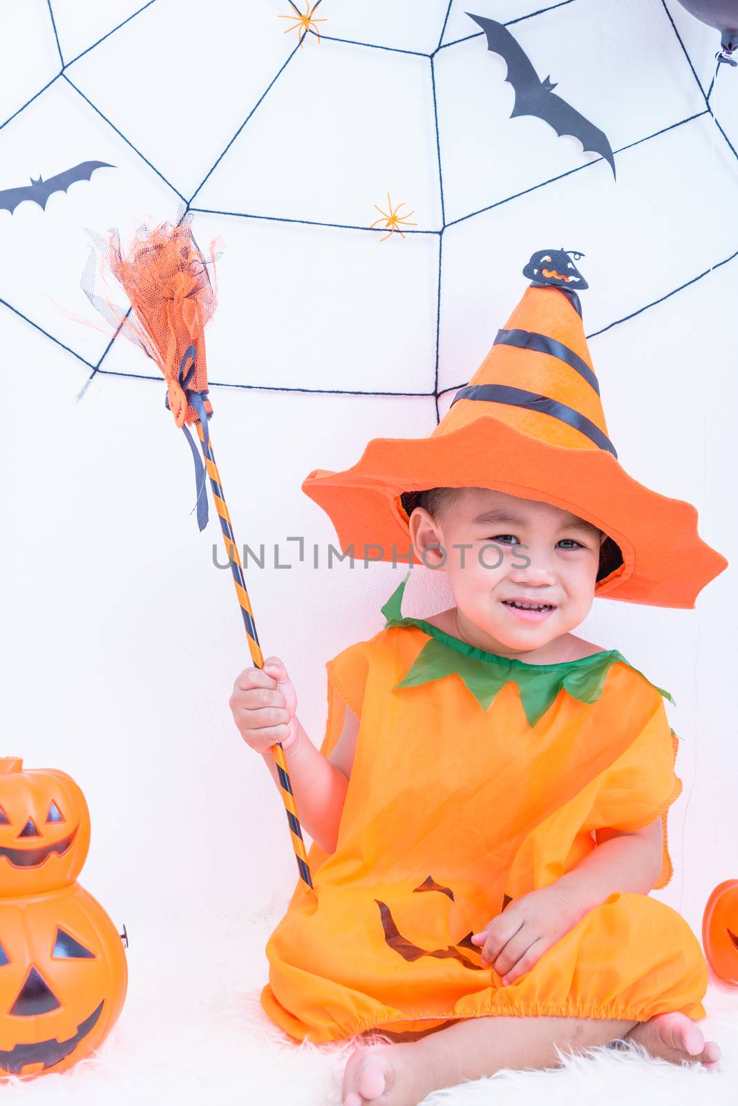 Funny happy little cute child boy in Halloween costume with orange pumpkin Jack with Cobweb in-home with Halloween party on white wall background, Happy Halloween day concept