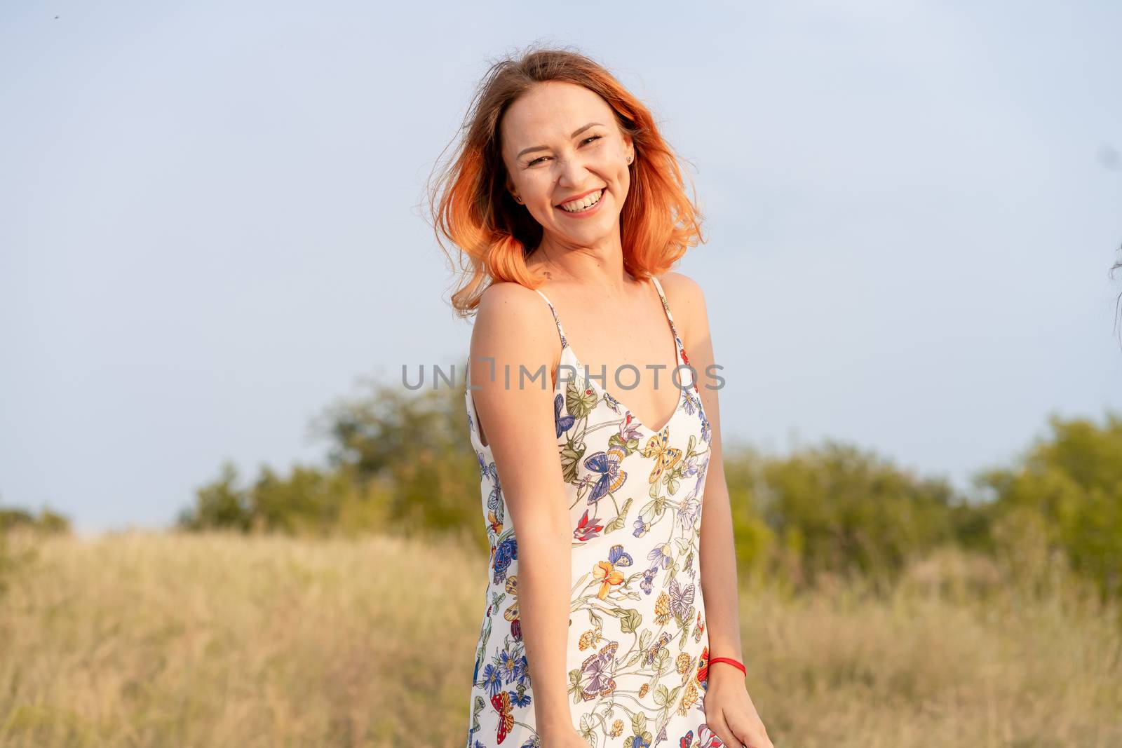 Beautiful red-haired girl is having fun and dancing in a field at sunset.