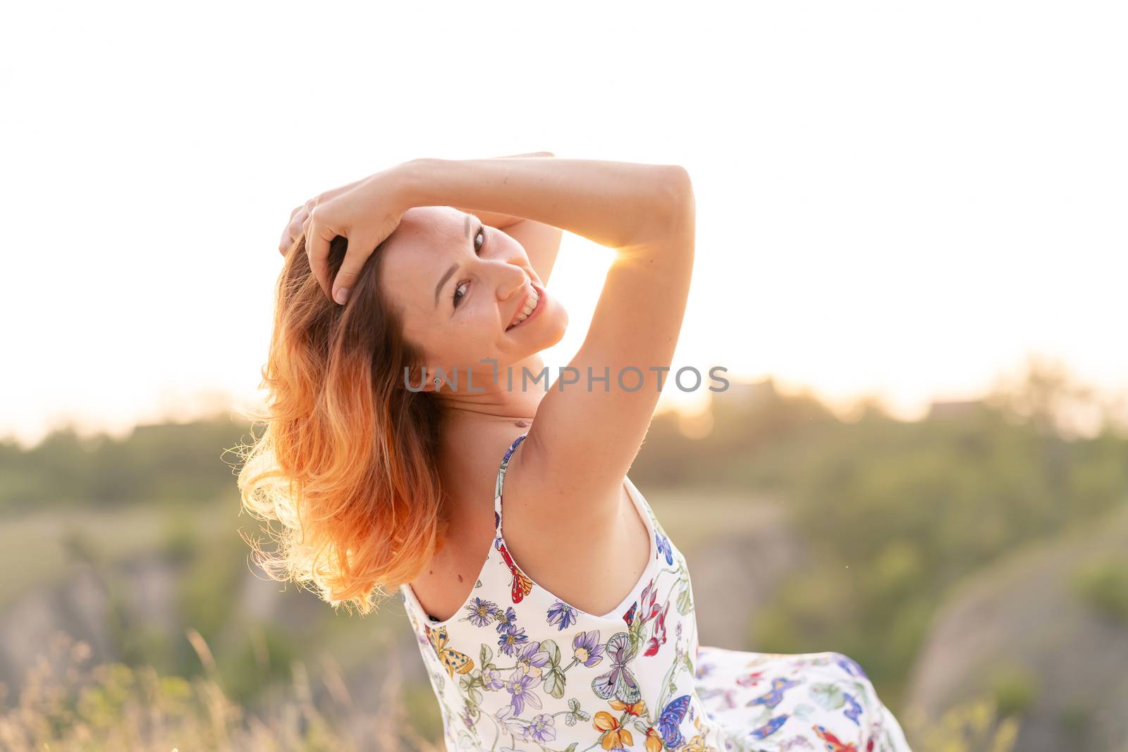 Tender beautiful red-haired girl enjoys the sunset in a field with a hill