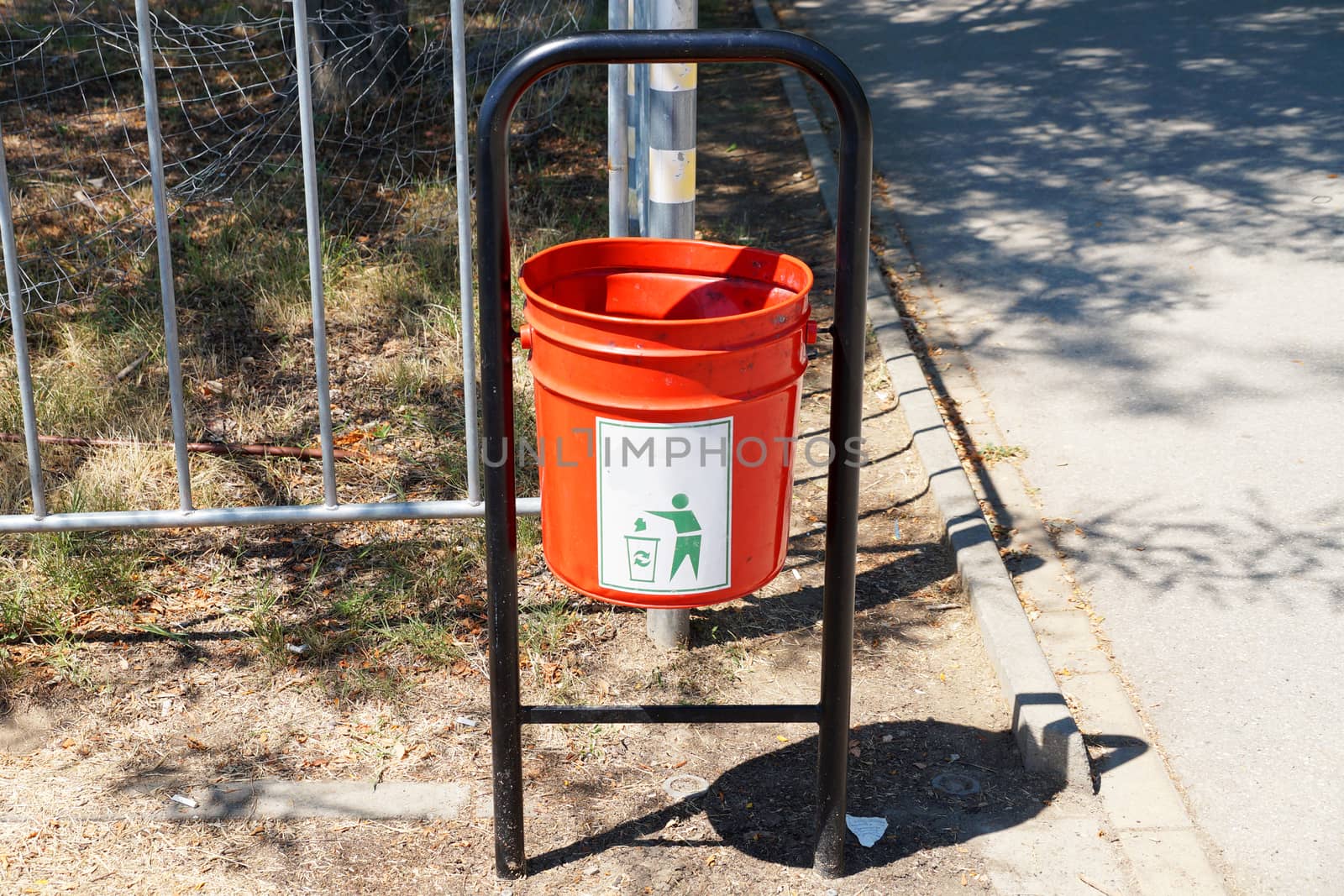 red metal trash can in the park close up by Annado