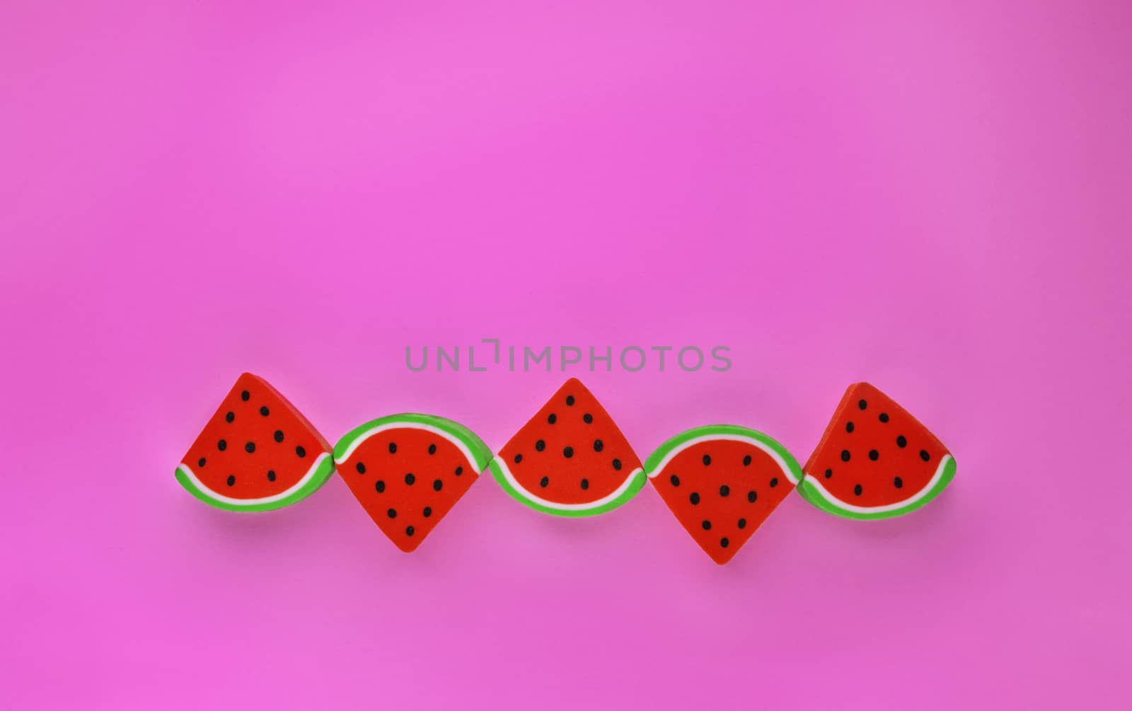A group of erasers shaped like sliced watermelon in a row on a colored background ,simple composition