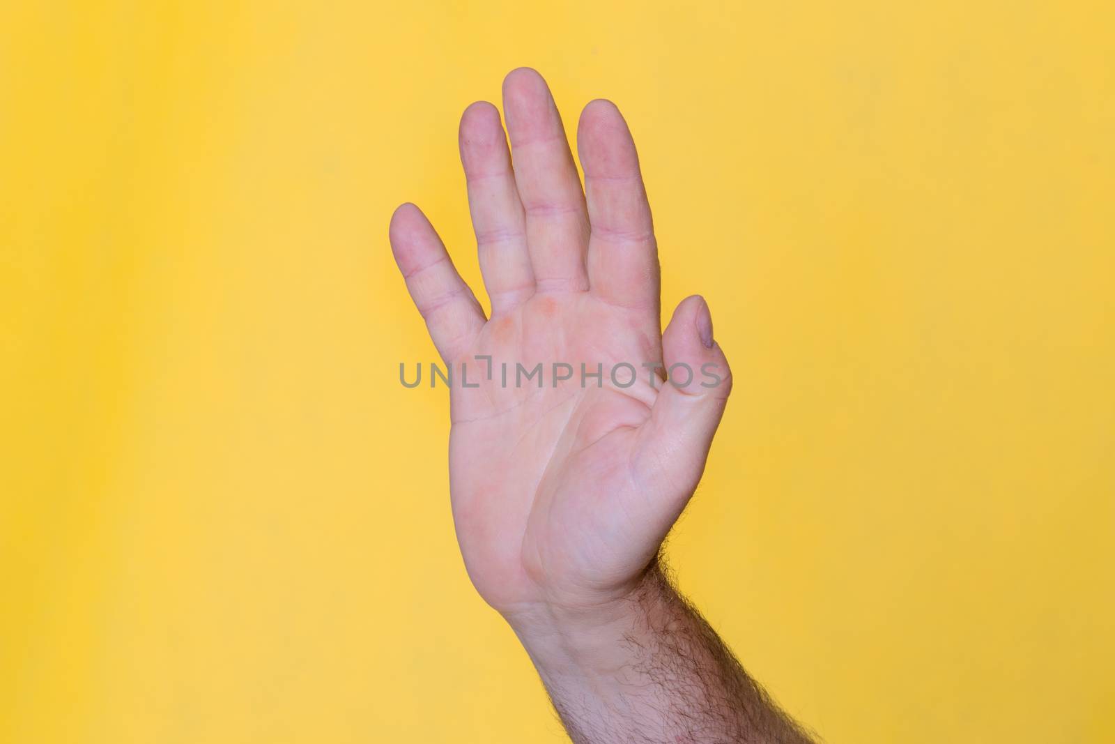 Man hand showing sign Stop on yellow background