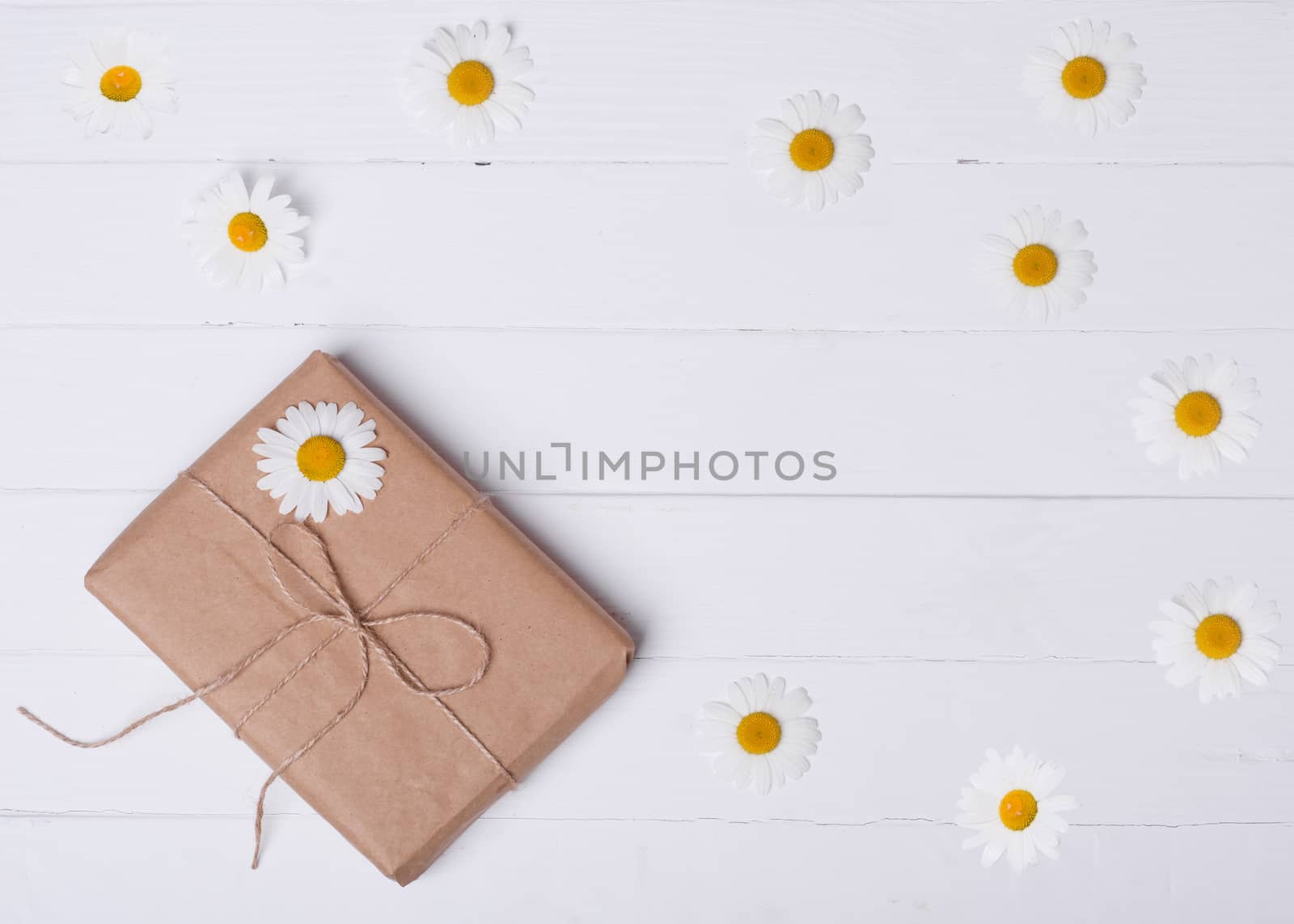 Gift box and daisy on a white wooden background