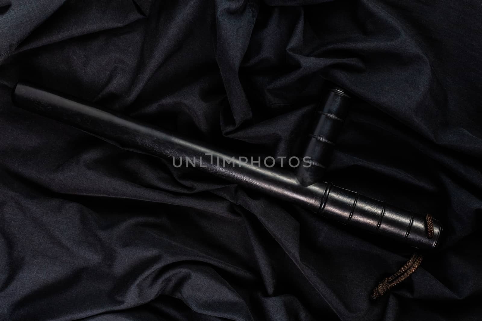 black rubber police baton on black shirt wrinkled cloth low-key flat lay.