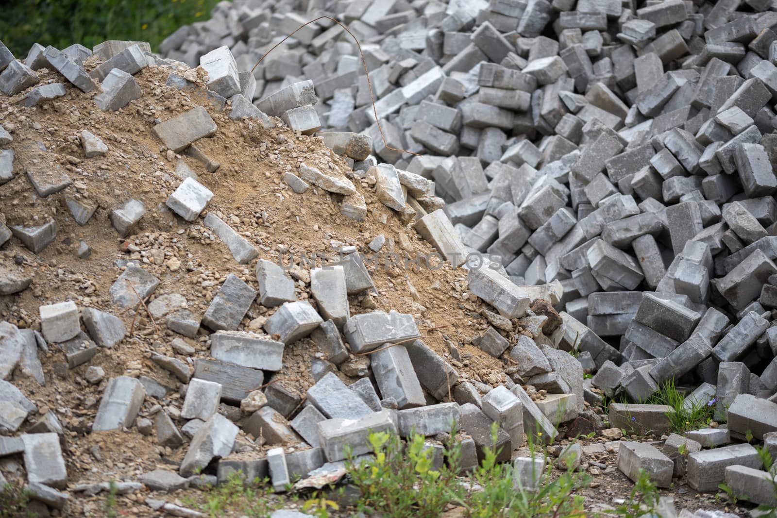 Pile of dismounted gray modern urban pavement bricks with selective focus. Result of russian government corruption in city infrastructure renovation. Piles hidden outside of city - in suburbs wasteland.