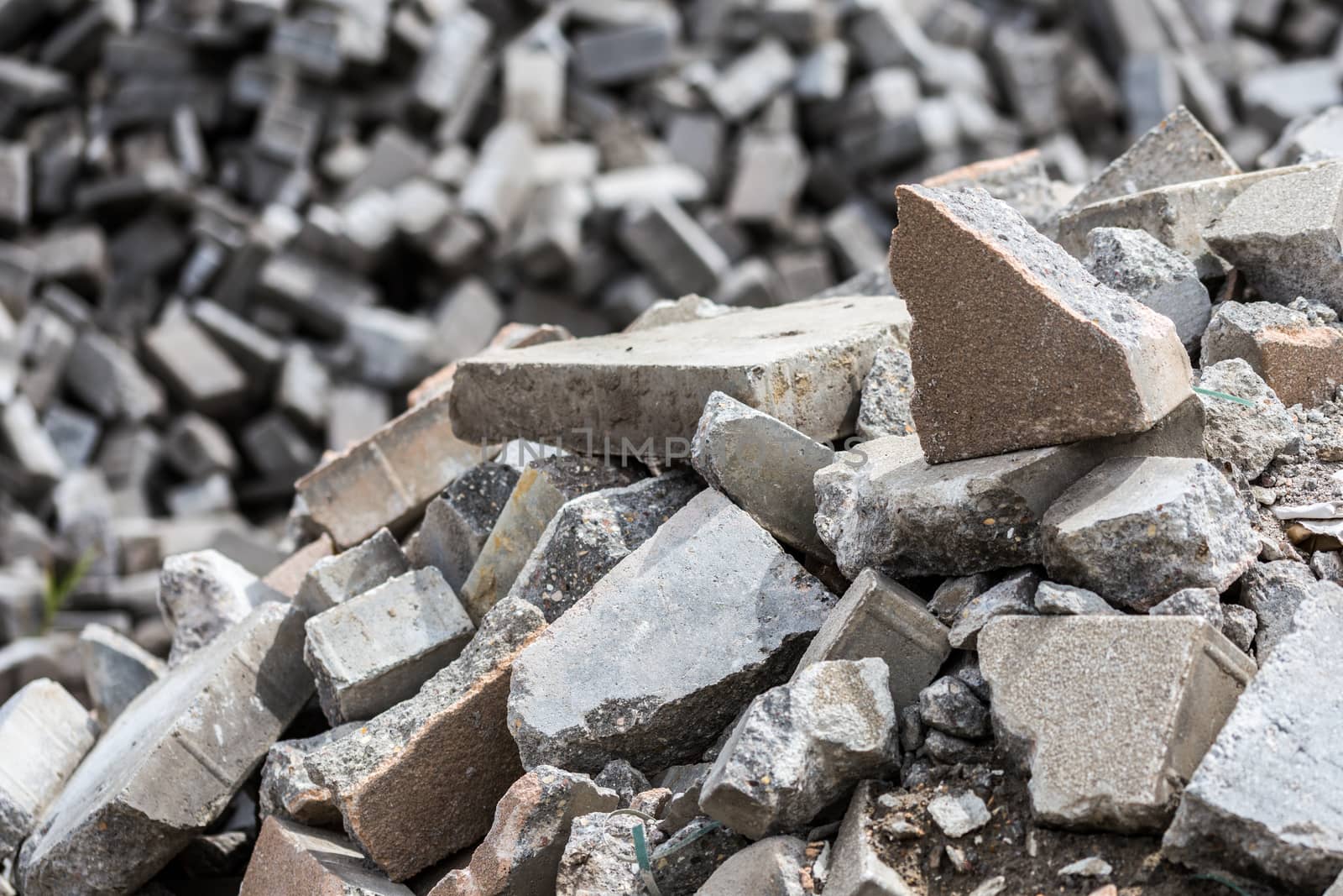 Pile of dismounted gray modern urban pavement bricks with selective focus. Result of russian government corruption in city infrastructure renovation. Piles hidden outside of city - in suburbs wasteland.
