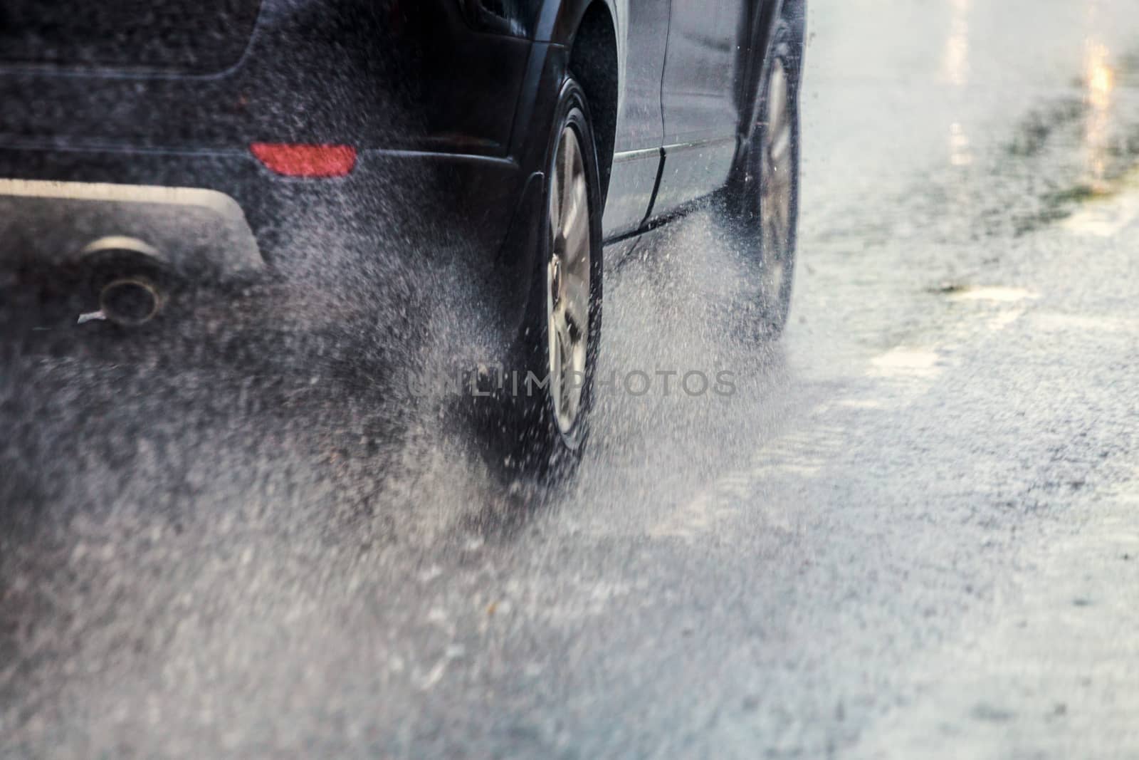 rain water splash flow from wheels of black car moving fast in daylight city with selective focus.