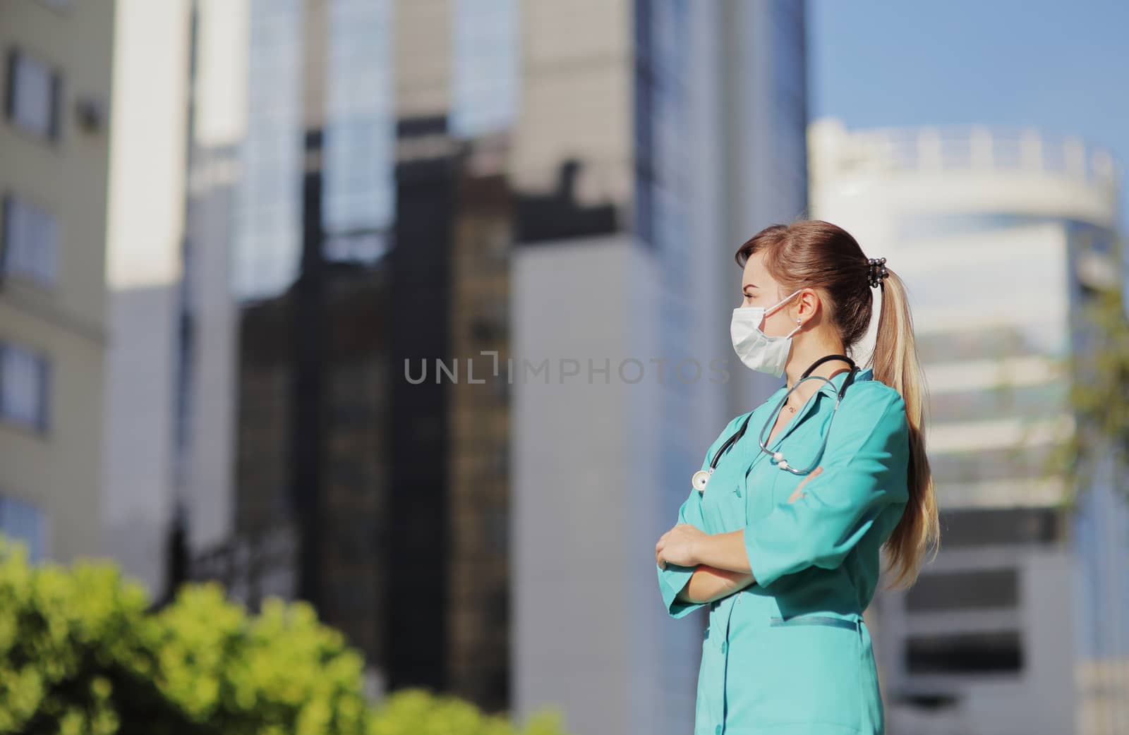 Female doctor, nurse wearing a protective face mask in the city. Skyscraper, sky by selinsmo