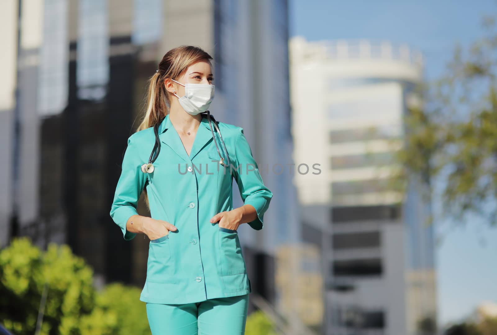 Female doctor, nurse wearing a protective face mask in the city. Skyscraper, sky by selinsmo