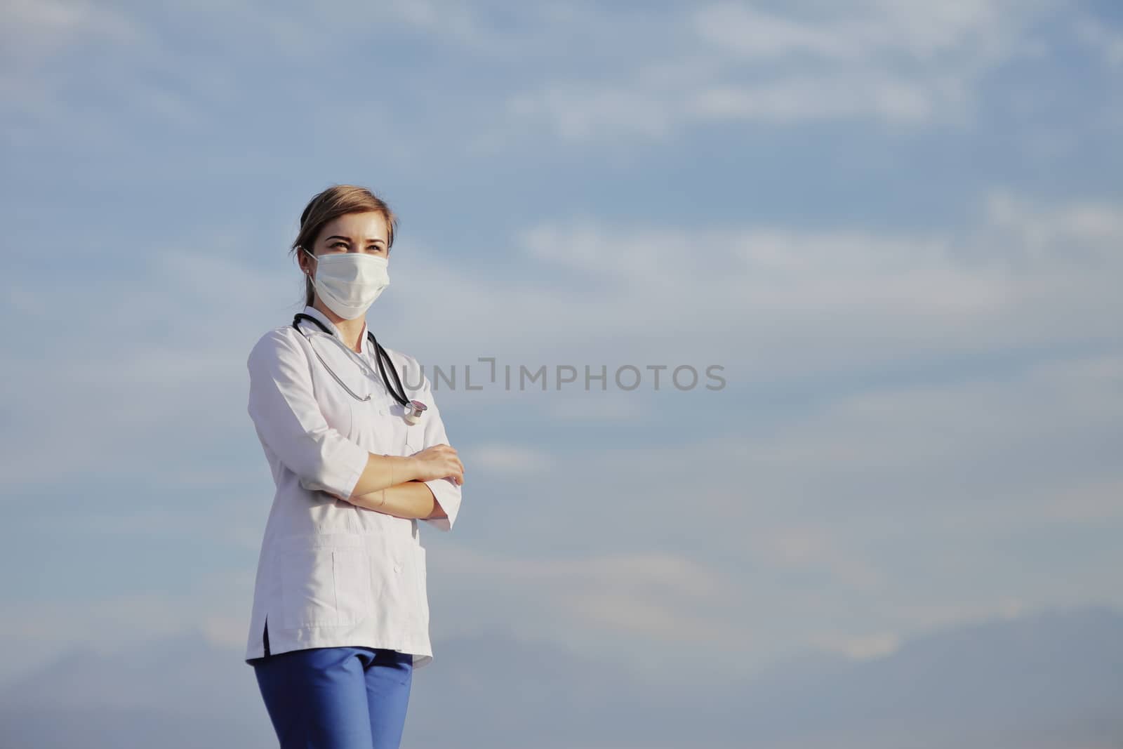 Female doctor, a nurse wearing a protective face mask against blue sky with clouds. Safety measures against the coronavirus. Prevention Covid-19 healthcare concept. Stethoscope. Woman, girl.