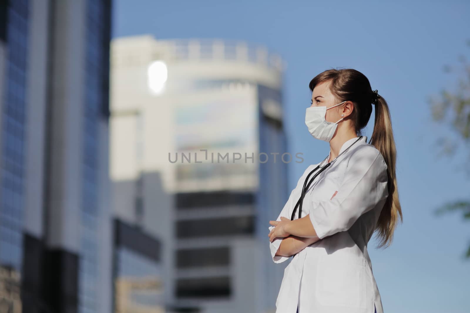 Female doctor, a nurse wearing a protective face mask in the city. Skyscraper, sky. Safety measures against the coronavirus. Prevention Covid-19 healthcare concept. Stethoscope. Woman, girl.