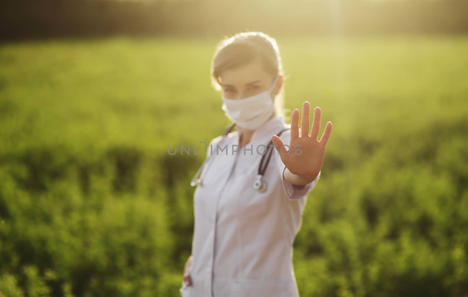A woman doctor in a medical face mask showing a stop pandemic gesture. by selinsmo