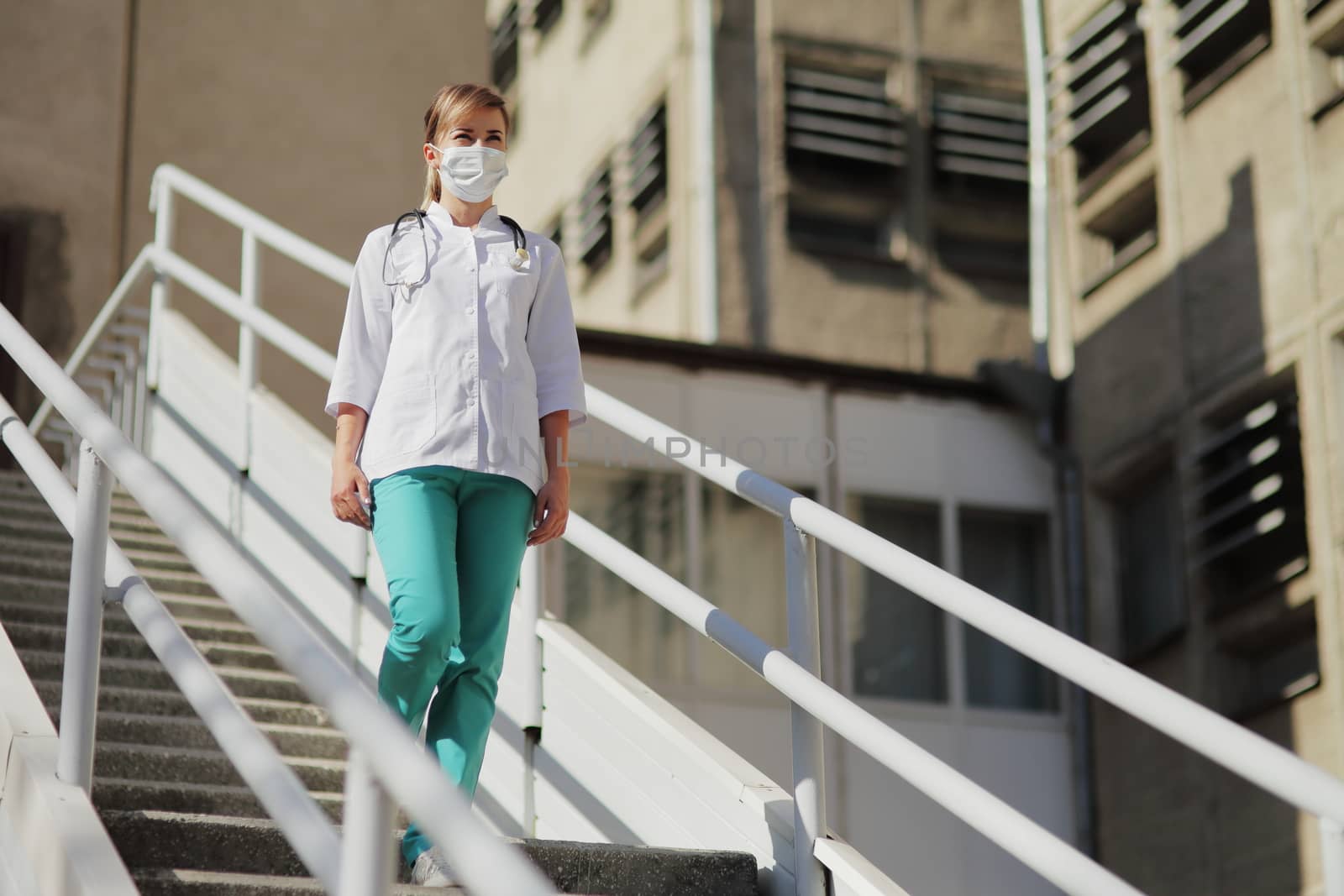 Female doctor or nurse in a protective face mask walking up the stairs. Safety measures against the coronavirus. Prevention Covid-19 healthcare concept. Stethoscope over the neck. Woman, girl.