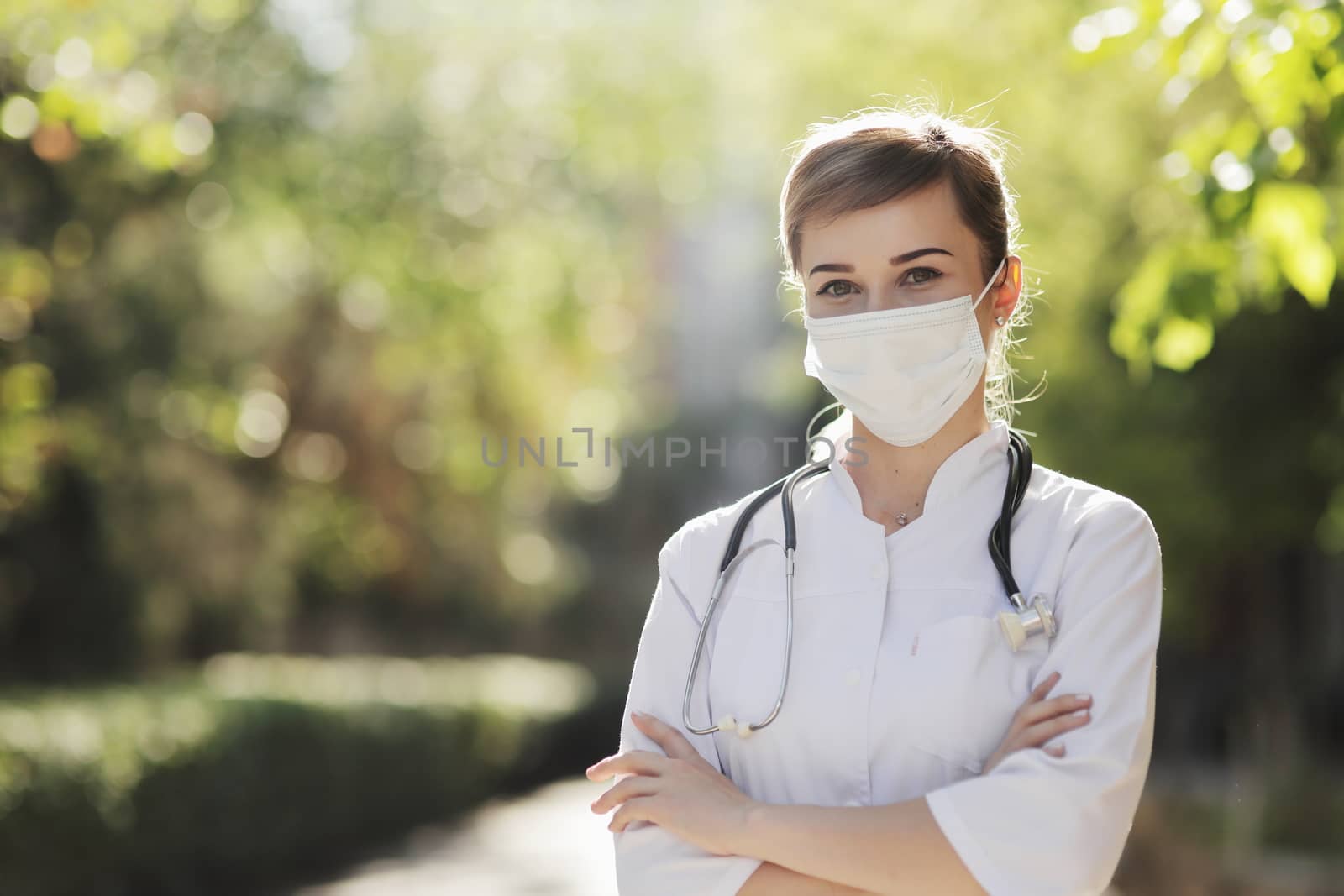 Woman doctor or nurse in a face protective mask in the park among the trees. by selinsmo