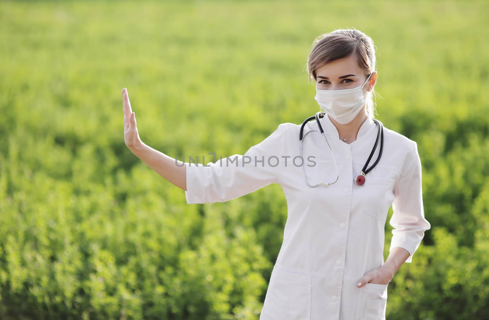 A woman doctor in a medical face mask showing a stop pandemic gesture. by selinsmo