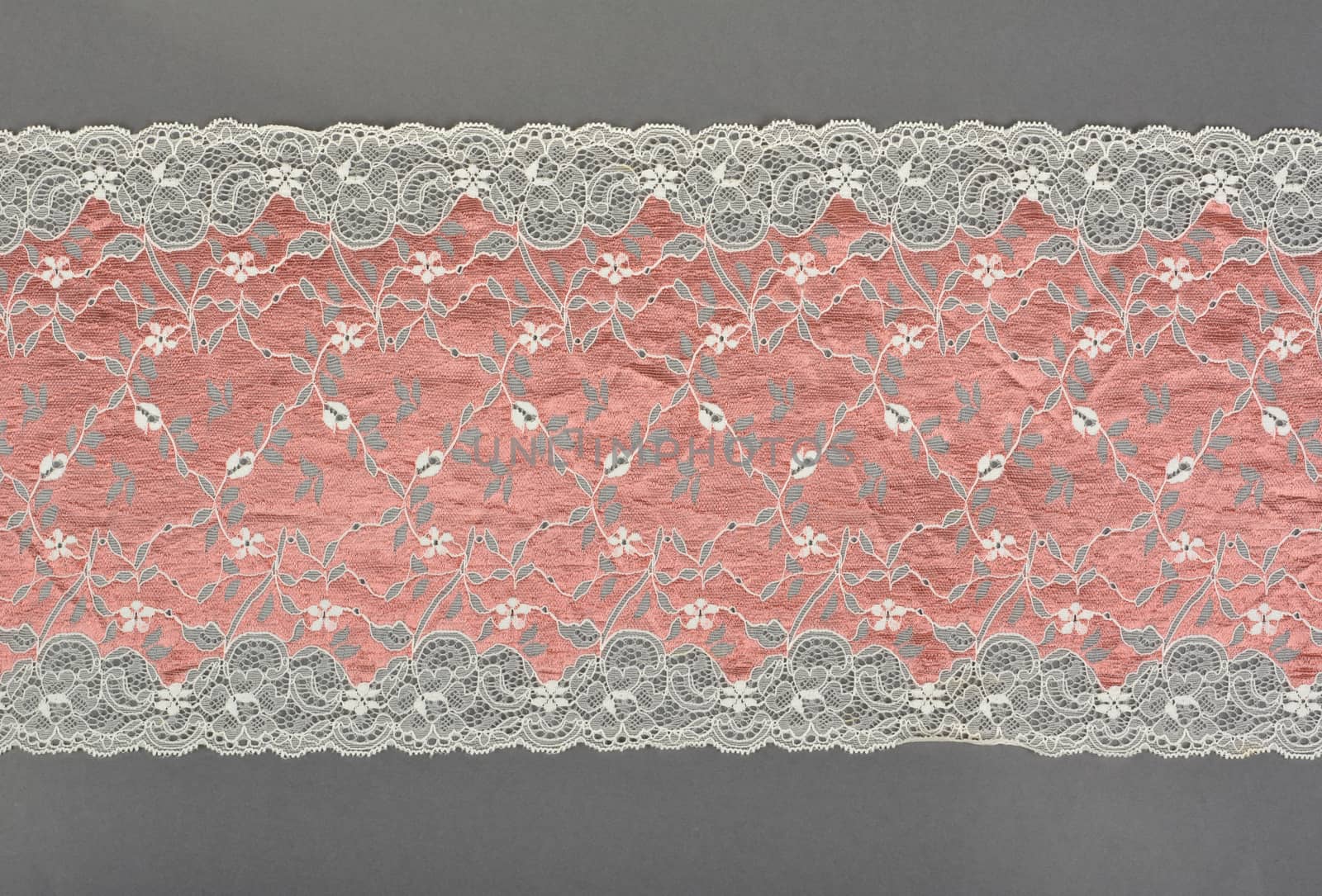 pink beige color straight strip of lace fabric on gray background. Elastic silk nylon braid border. use clothes linen decoration. repeating pattern and interweaving threads. texture for websites