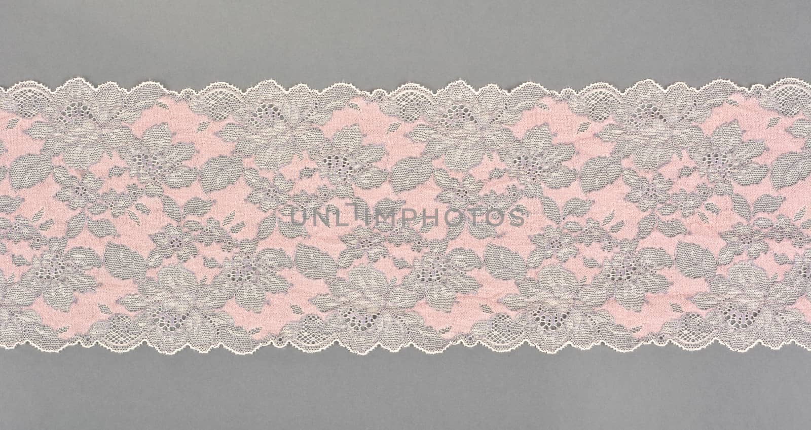 pink beige color straight strip of lace fabric on gray background. Elastic silk nylon braid border. use clothes linen decoration. repeating pattern and interweaving threads. texture for websites