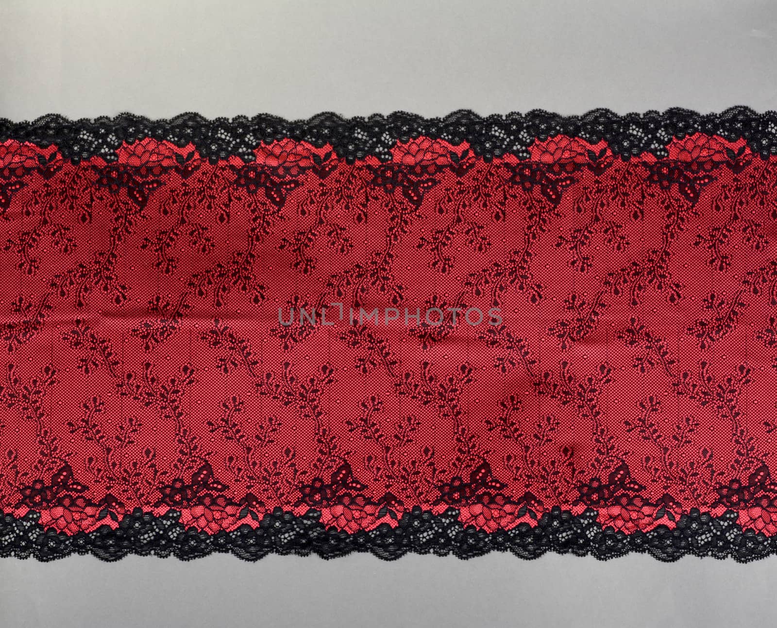 red black color straight strip of lace fabric on gray background. Elastic silk nylon braid border. use clothes linen decoration. repeating pattern and interweaving threads. texture for websites