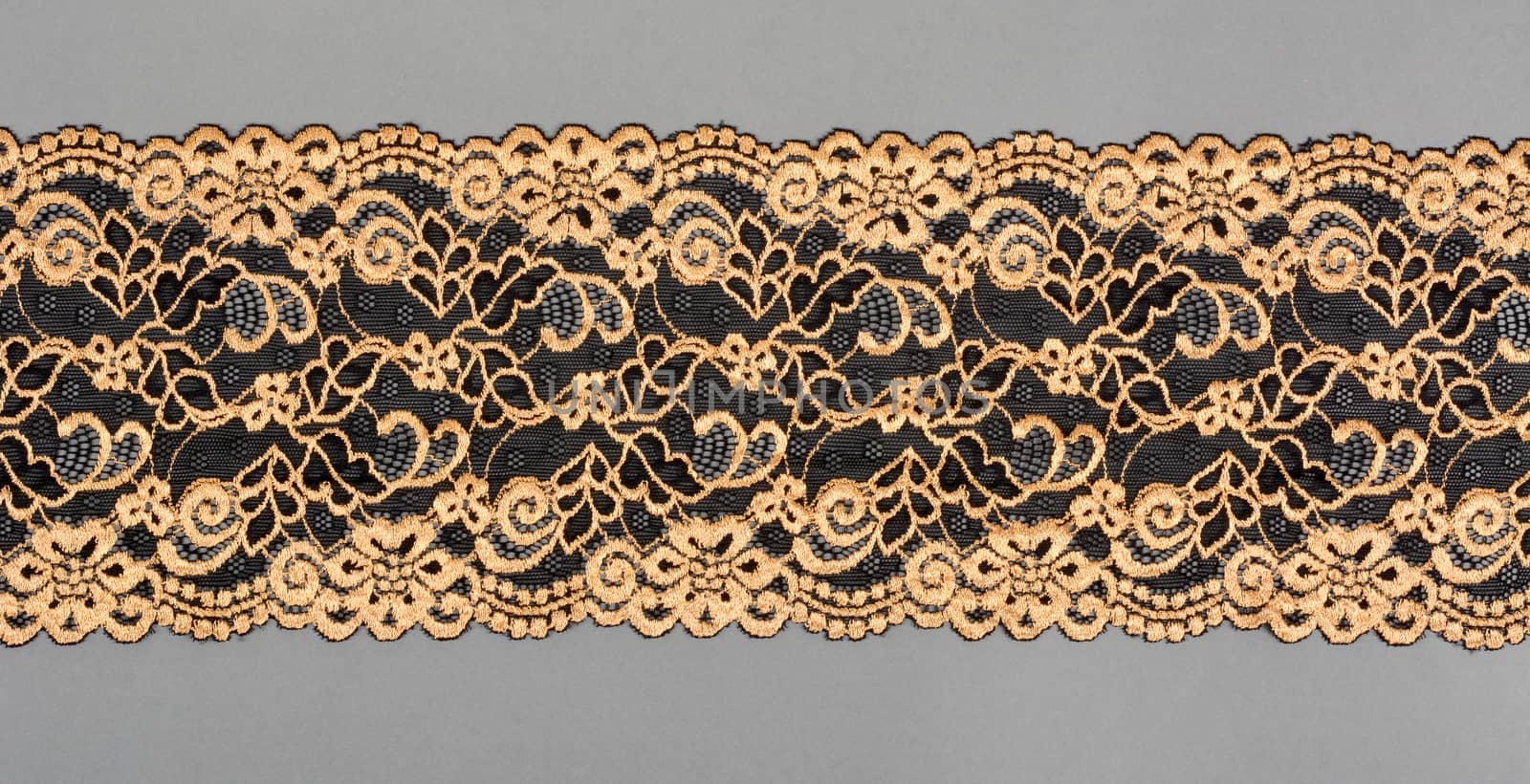 gold, black color straight strip of lace fabric on gray background. Elastic silk nylon braid border. use clothes linen decoration. repeating pattern and interweaving threads. texture for websites