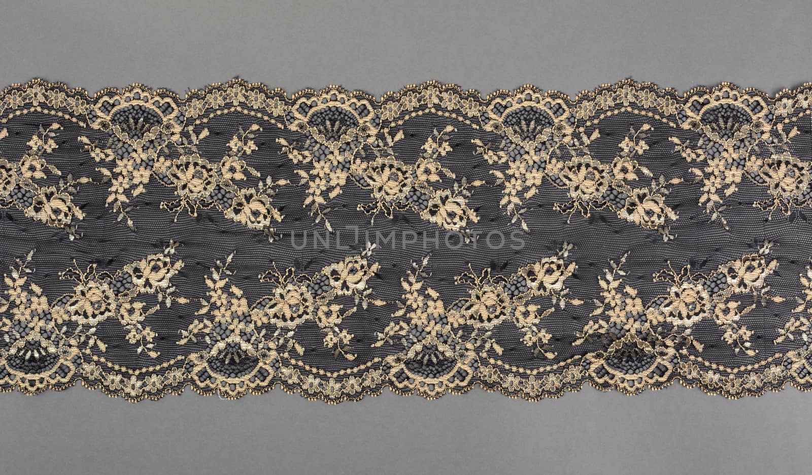 black beige color straight strip of lace fabric on gray background. Elastic silk nylon braid border. use clothes linen decoration. repeating pattern and interweaving threads. texture for websites