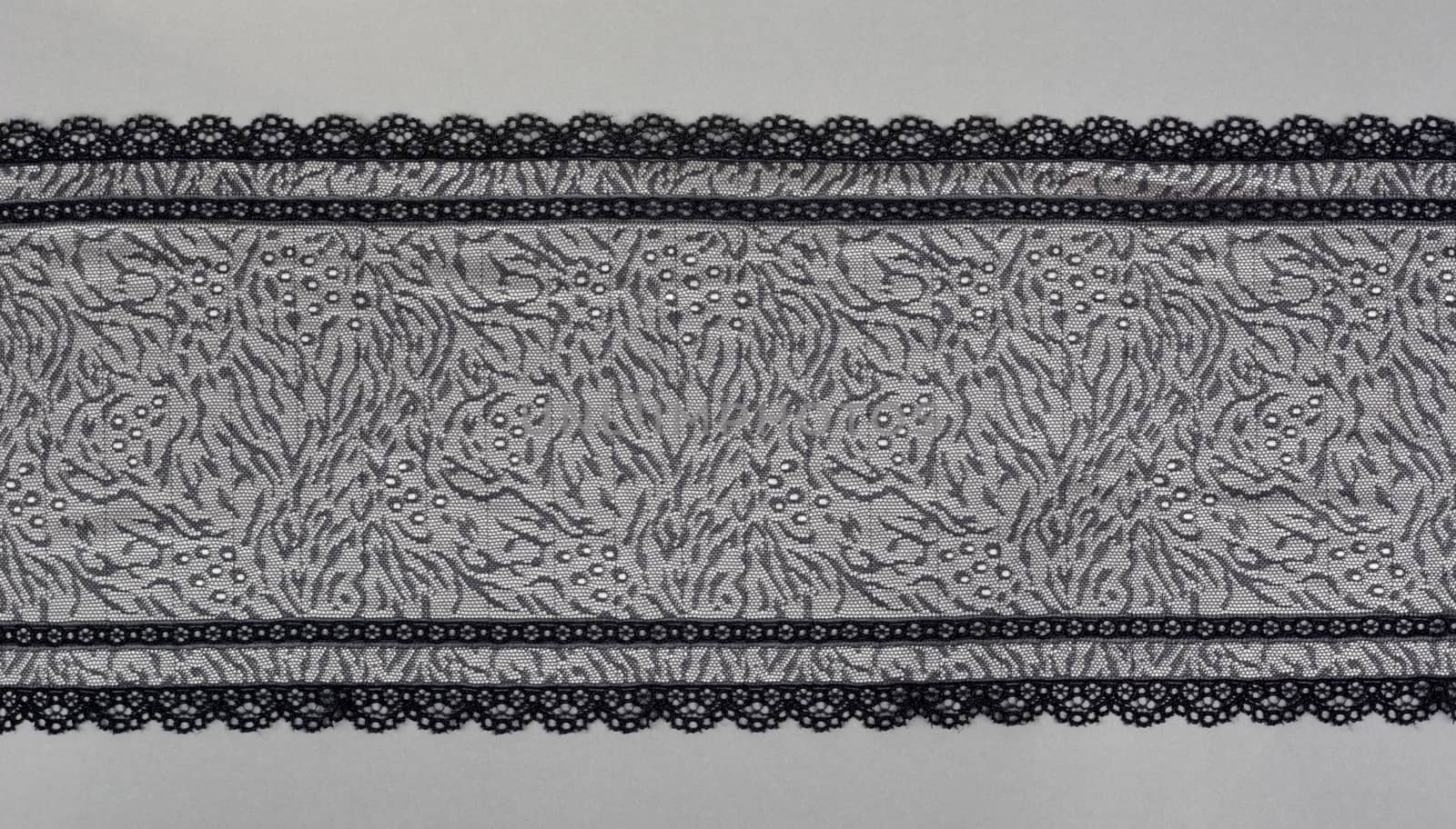 black gray color straight strip of lace fabric on gray background. Elastic silk nylon braid border. use clothes linen decoration. repeating pattern and interweaving threads. texture for websites