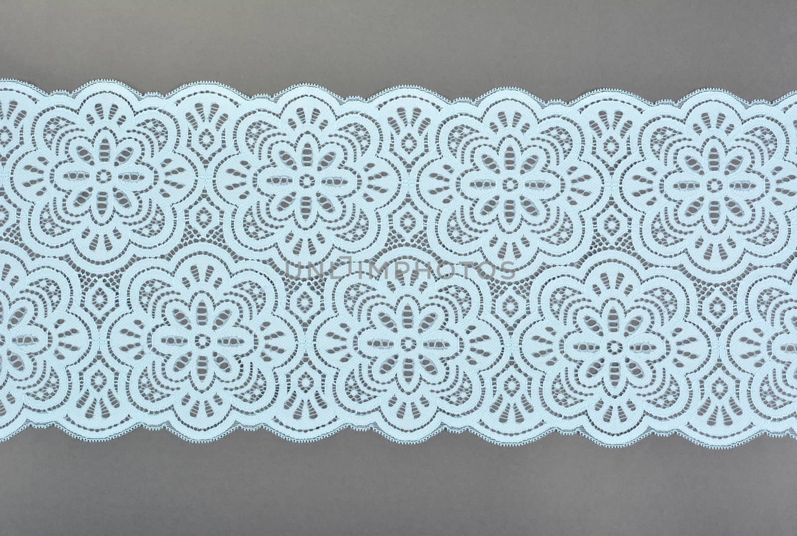 blue color straight strip of lace fabric on gray background. Elastic silk nylon braid border. use clothes linen decoration. repeating pattern and interweaving threads. texture for websites