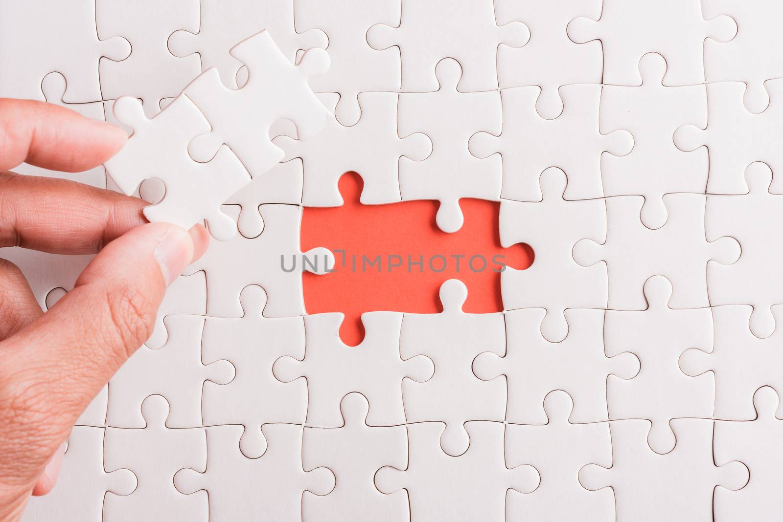 Top view flat lay of hand-holding last piece white paper jigsaw puzzle game last pieces put to place for solve problem complete mission, studio shot on a pink background, quiz calculation concept