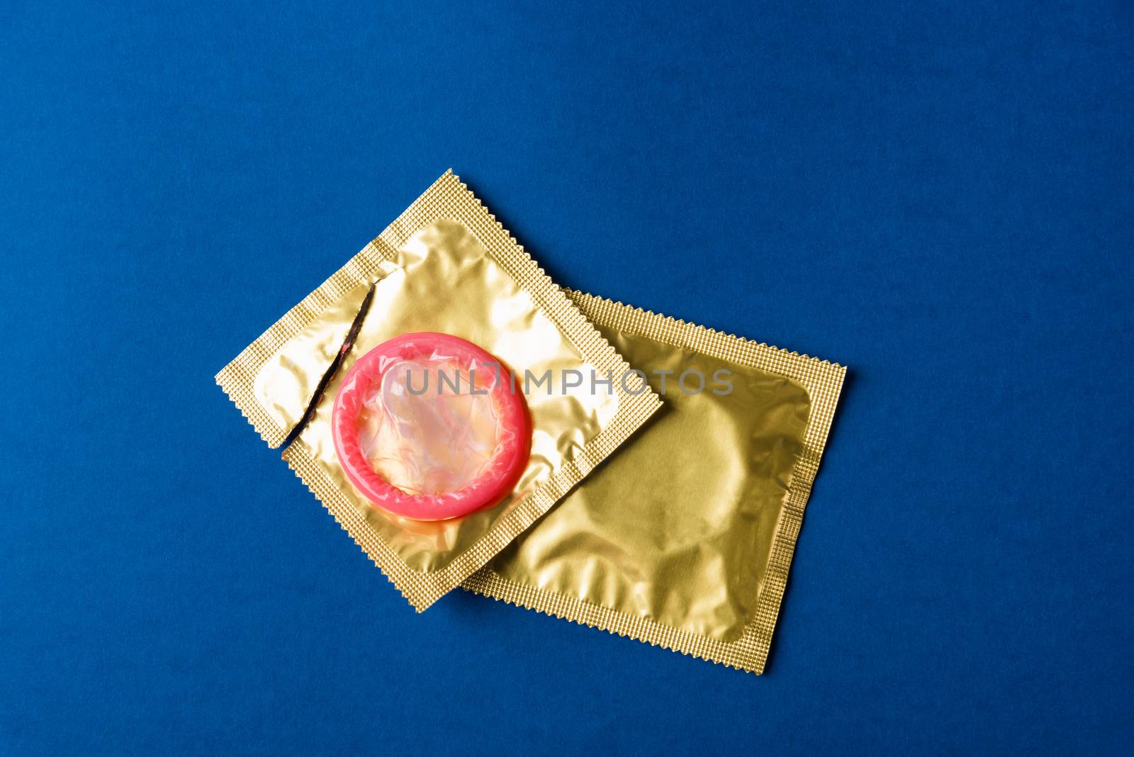World sexual health or Aids day, Top view flat lay condom in wrapper pack is tear open, studio shot isolated on a dark blue background, Safe sex and reproductive health concept