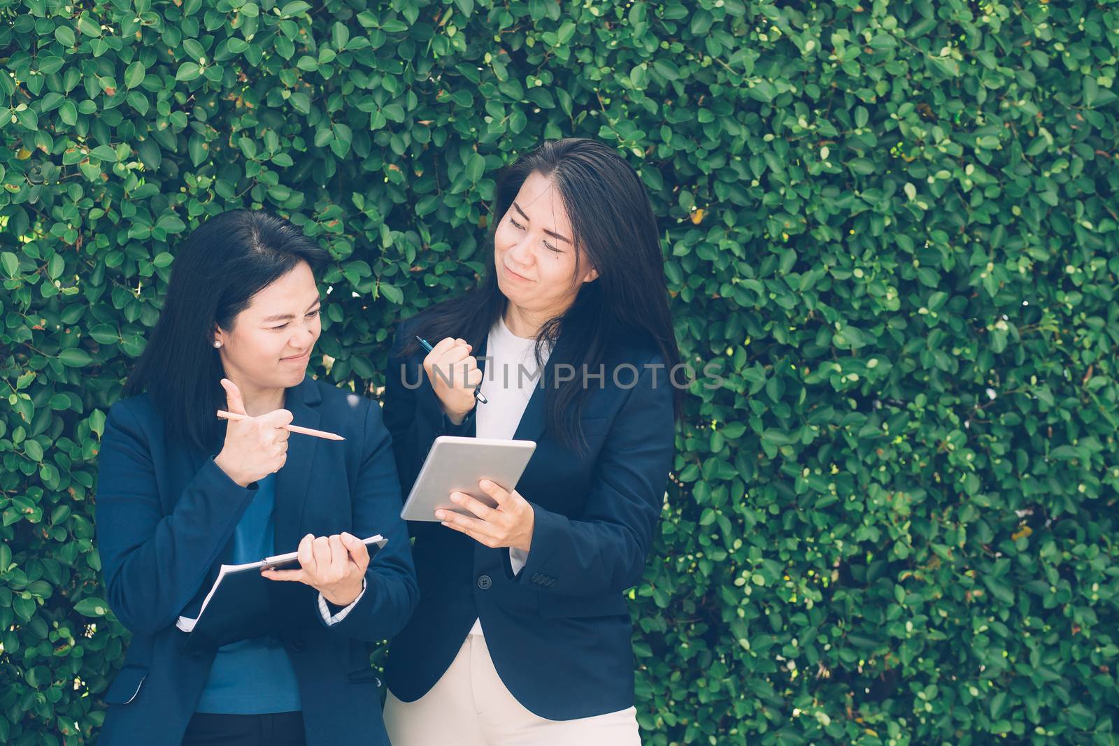Two business people discussing information on a tablet-and taking notes as they work together as a team in the garden.
