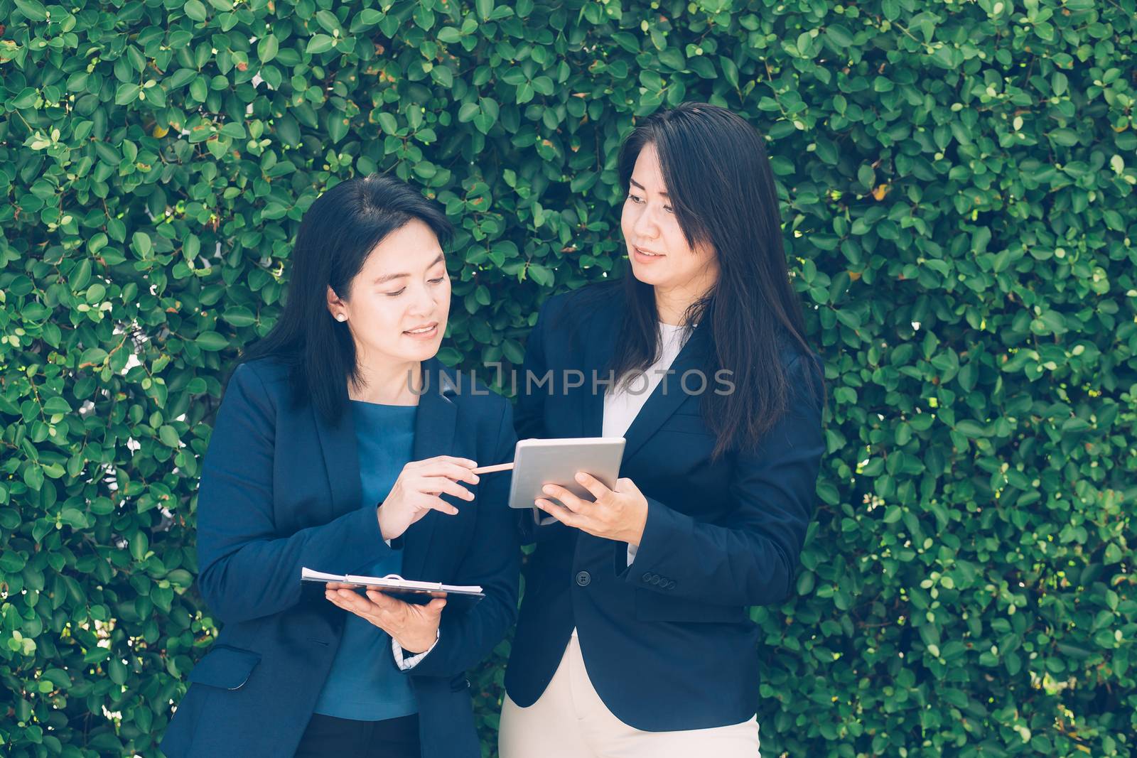 Two business people discussing information on a tablet-and taking notes as they work together as a team in the garden.