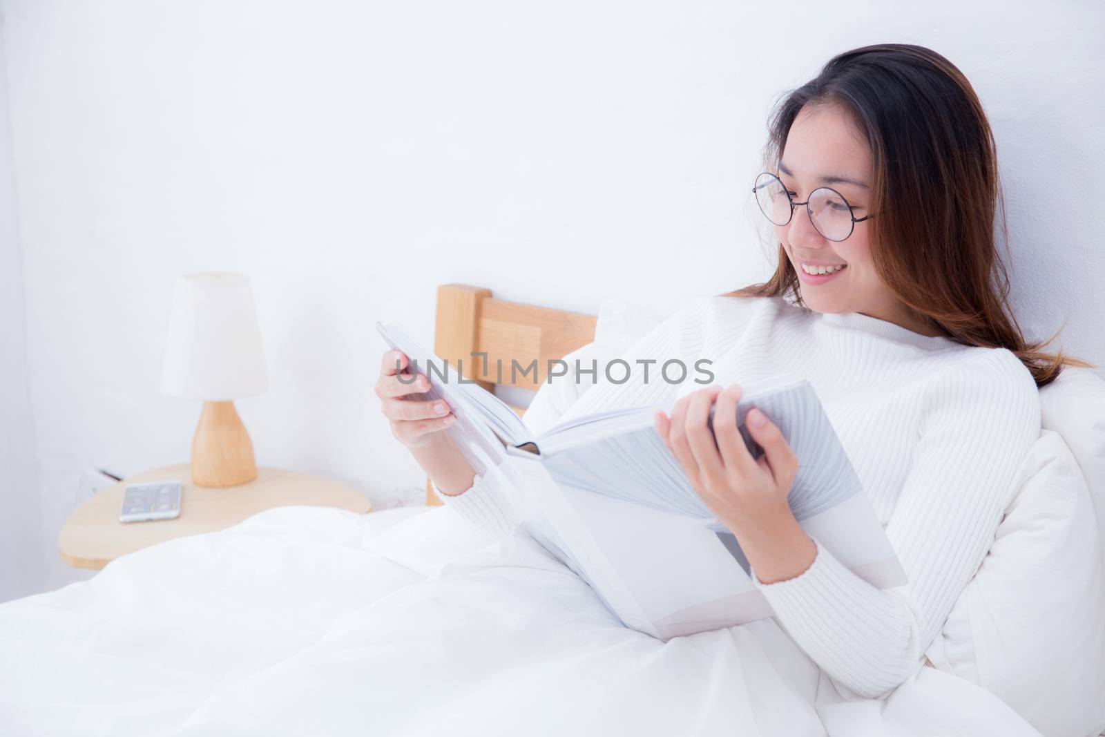 Asian woman reading a book and smiling in bedroom. lifestyle con by nnudoo