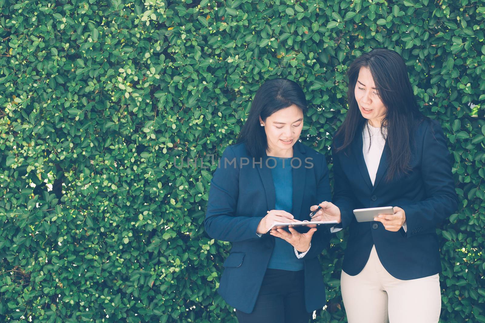 Two business people discussing information on a tablet-and taking notes as they work together as a team in the garden.