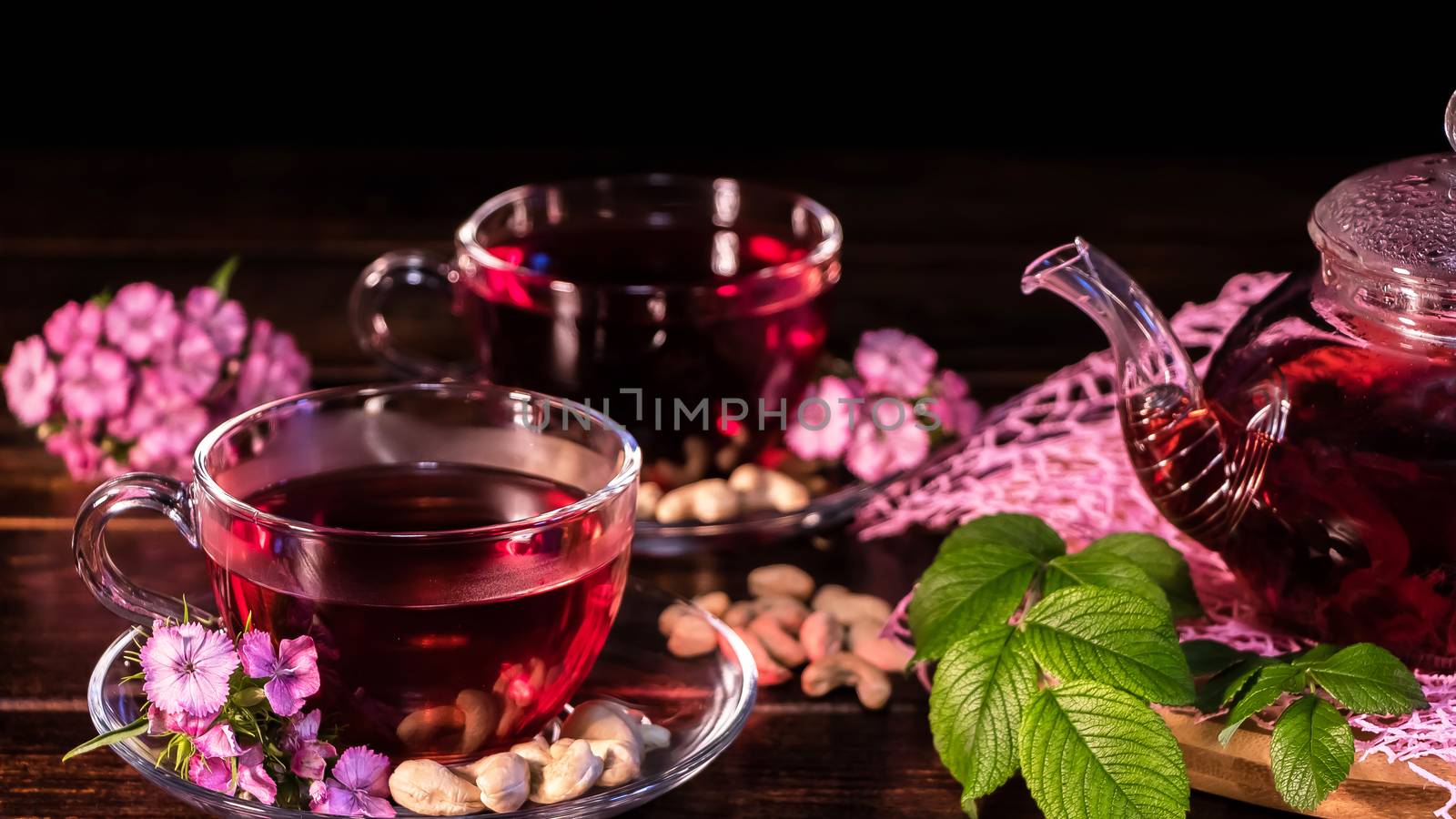 Green tea leaves or leaves of medicinal herbs lie on the table with a teapot and mugs of red tea, cashew nuts and clove flowers. Tea parties, tea traditions and ceremonies. Zen traditions of the East