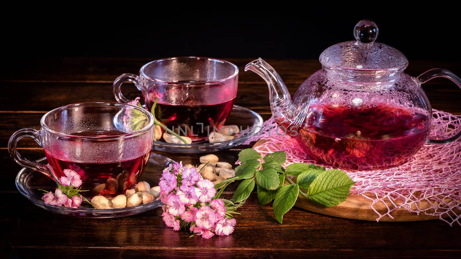 Tea parties, tea traditions and ceremonies. Zen traditions of the East.Green tea leaves or leaves of medicinal herbs lie on the table with a teapot and mugs of red tea, cashew nuts and clove flowers